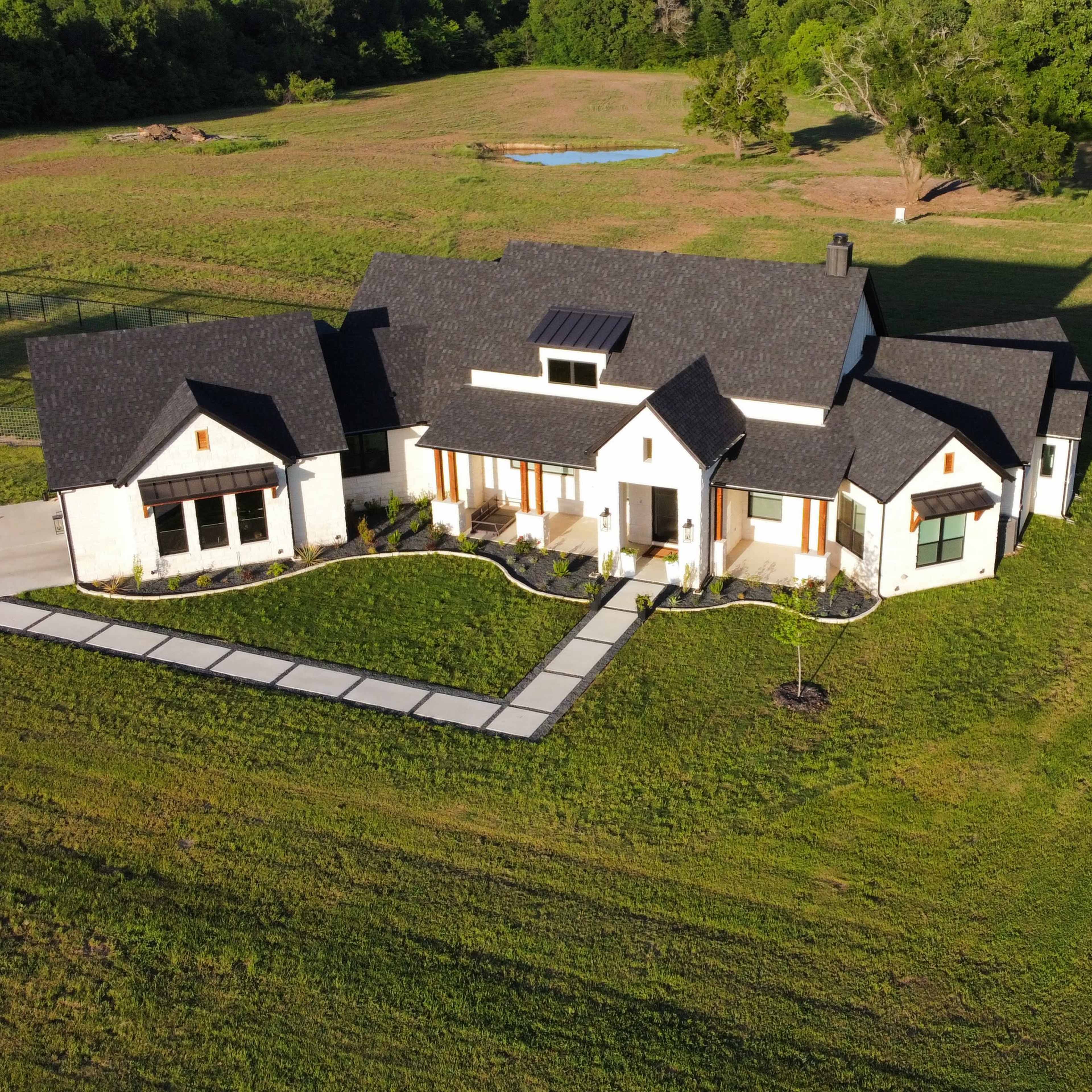 A modern, single-story house with a large lawn and a paved walkway leading to the entrance.