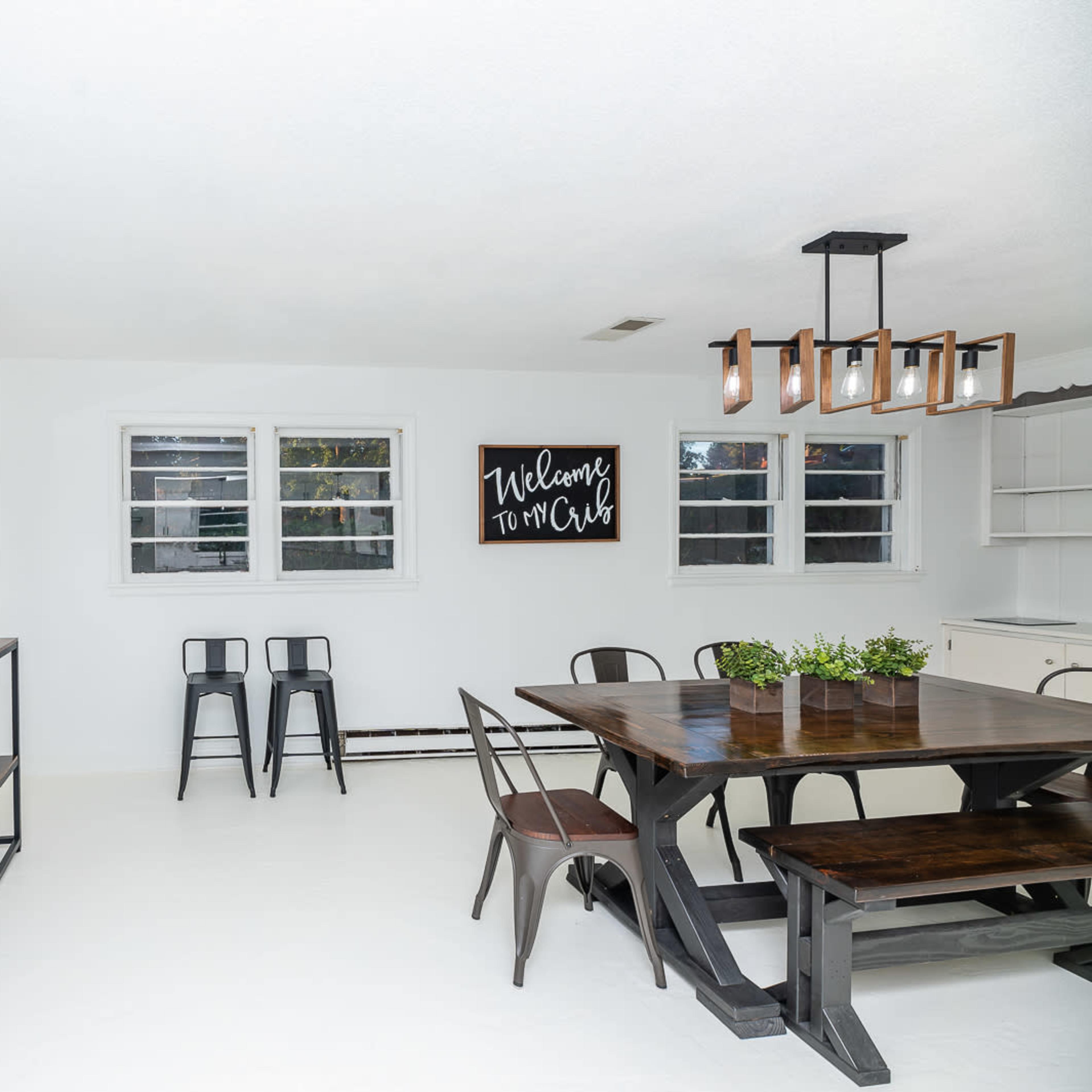 A bright dining area featuring a wooden table, black metal chairs, a console table against the wall, and framed wall art.