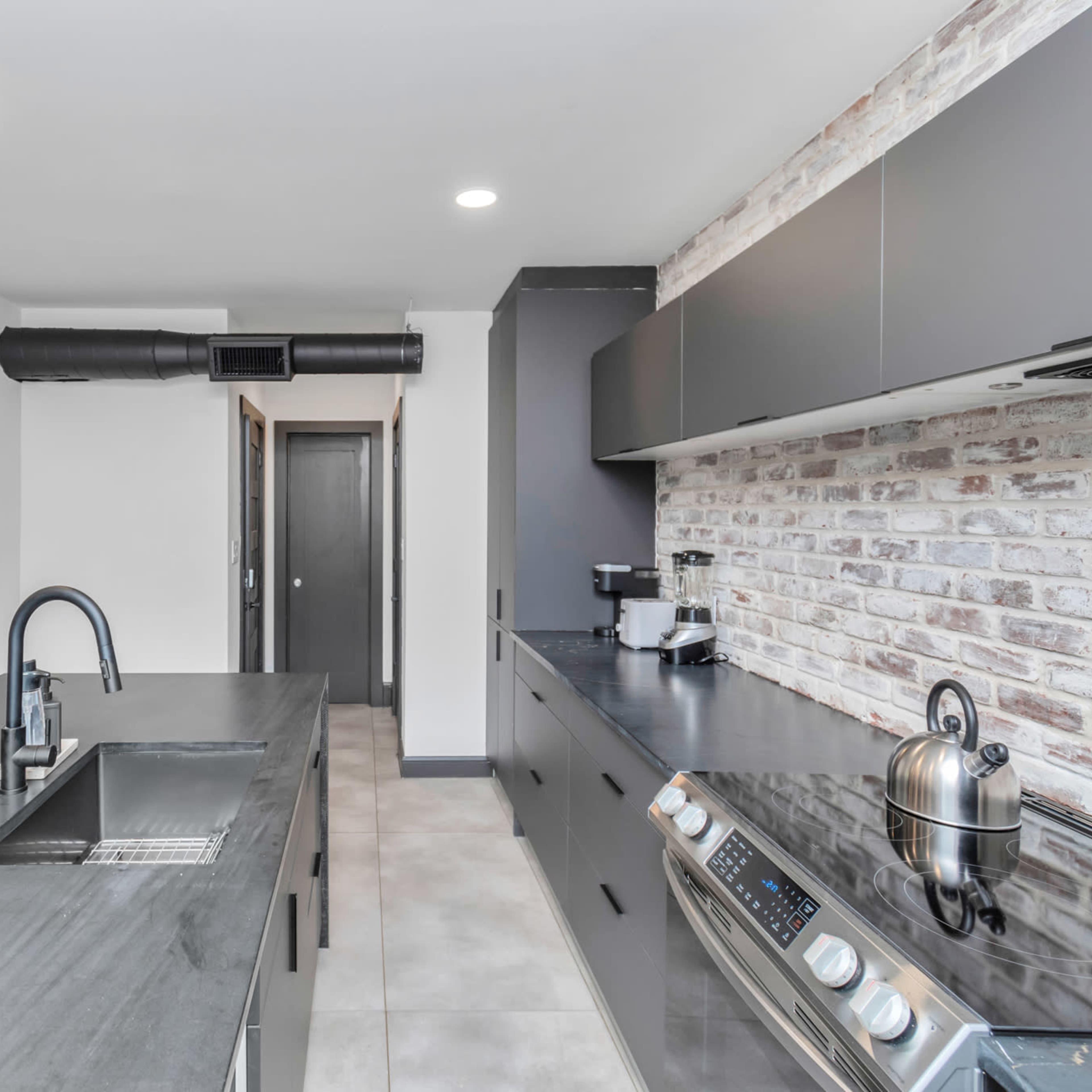 A modern kitchen featuring a large island with a sink, stainless steel appliances, and a brick accent wall.