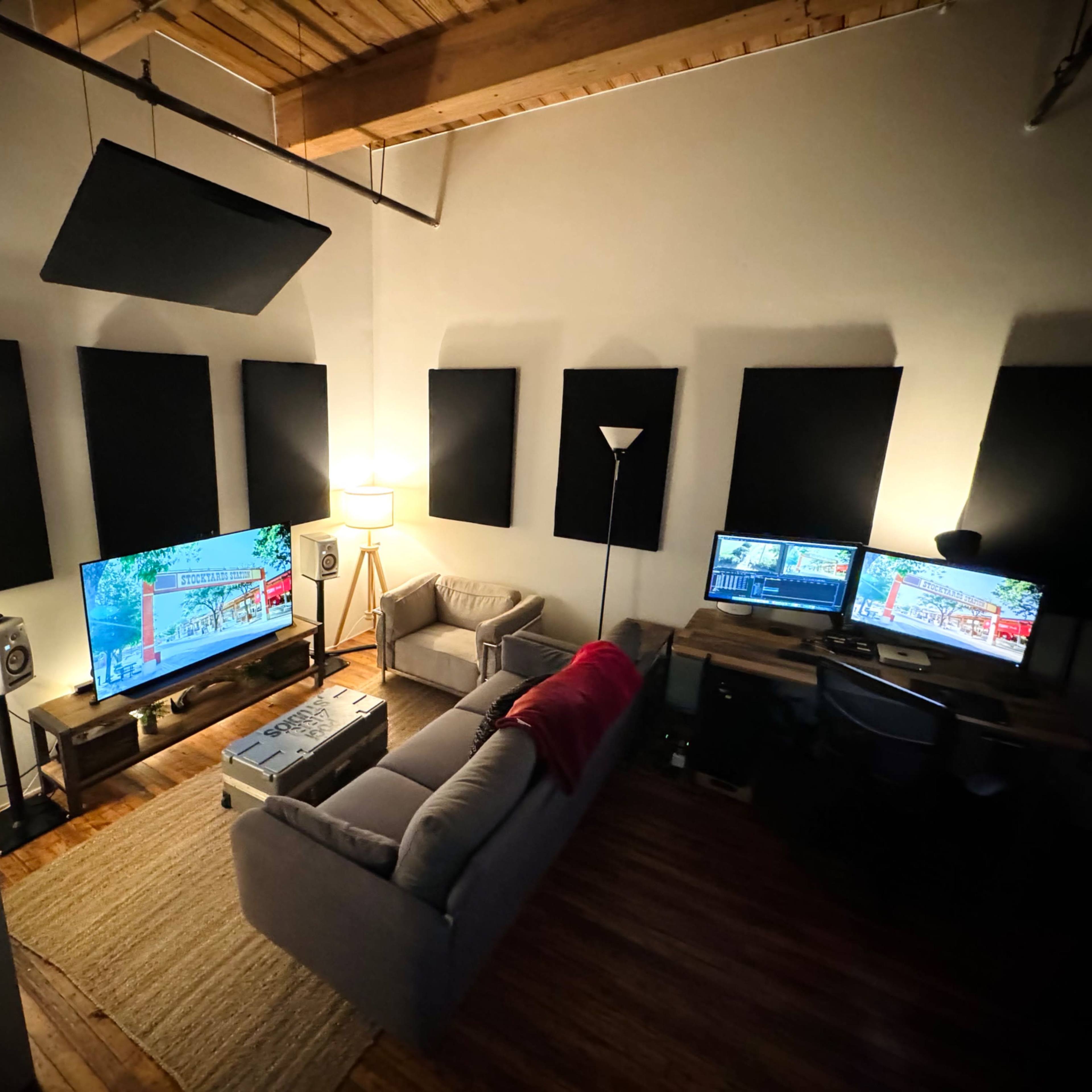 A cozy room features a couch, two televisions, a desk with a computer, and soundproofing panels on the walls.