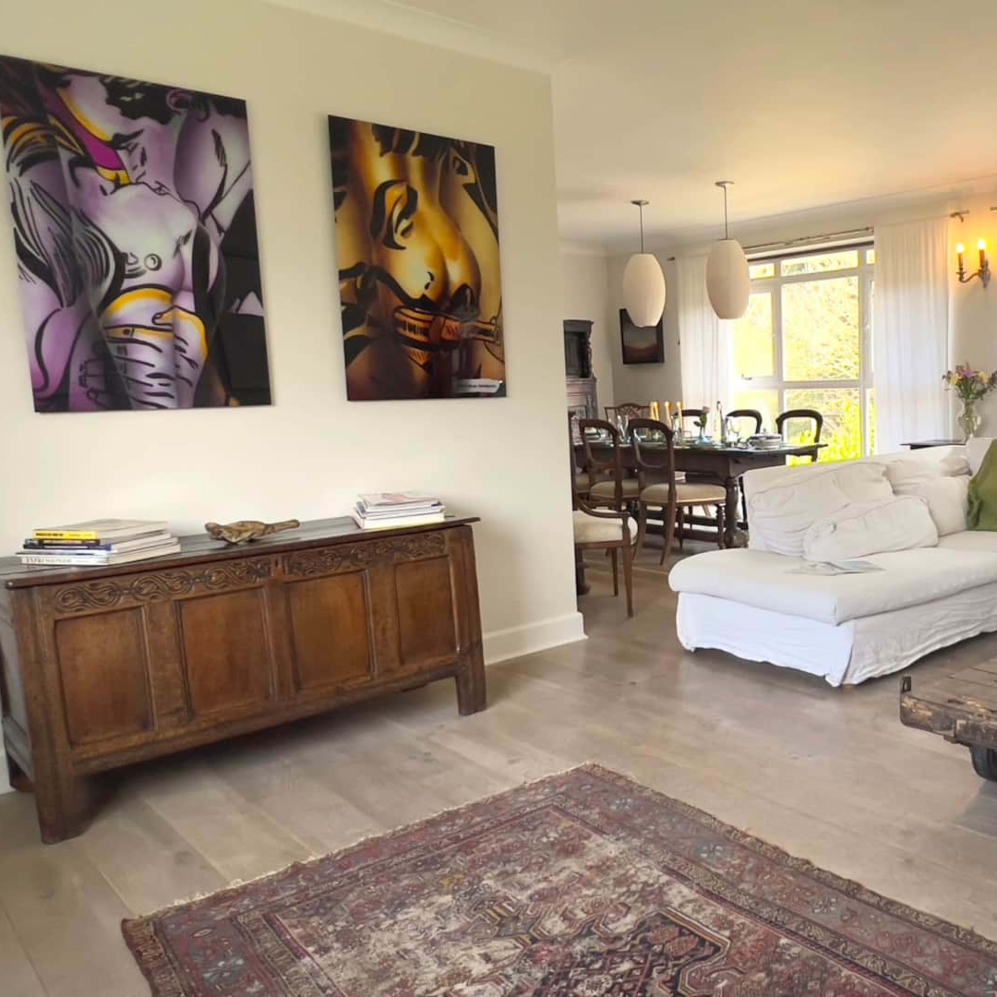 A bright living room features a white sectional sofa, a wooden coffee table, and artwork on the walls, with windows allowing natural light to enter.