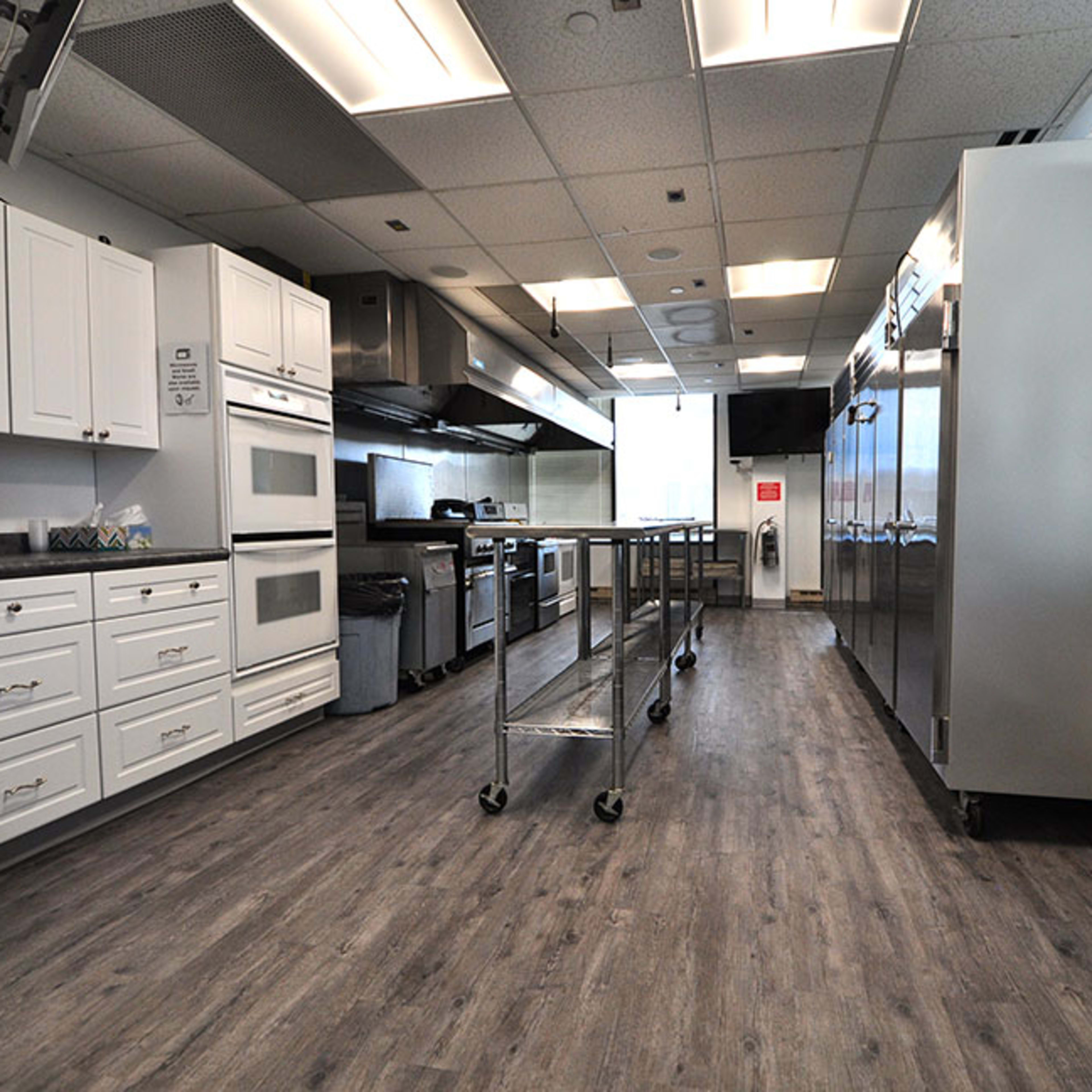 A modern kitchen with white cabinets, stainless steel appliances, and a series of metal carts positioned along the center of the space.