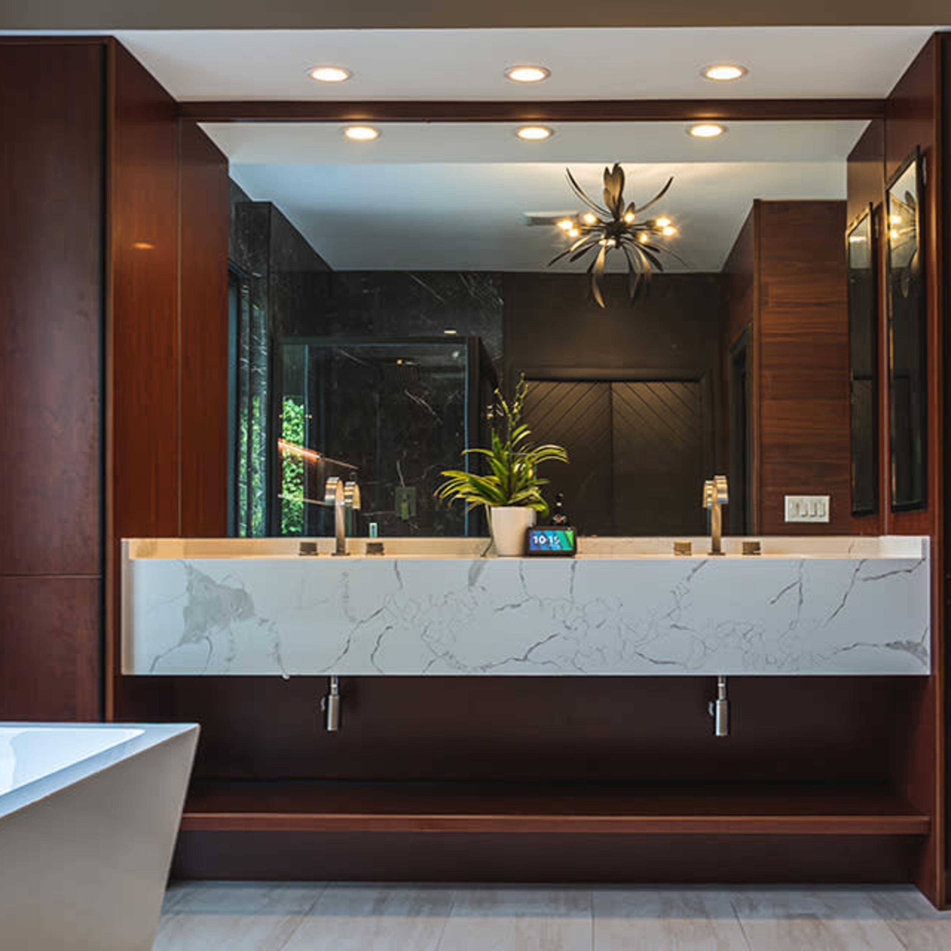 A modern bathroom features a dual sink vanity with a marble countertop and contemporary fixtures, complemented by a stylish light fixture and a large mirror.
