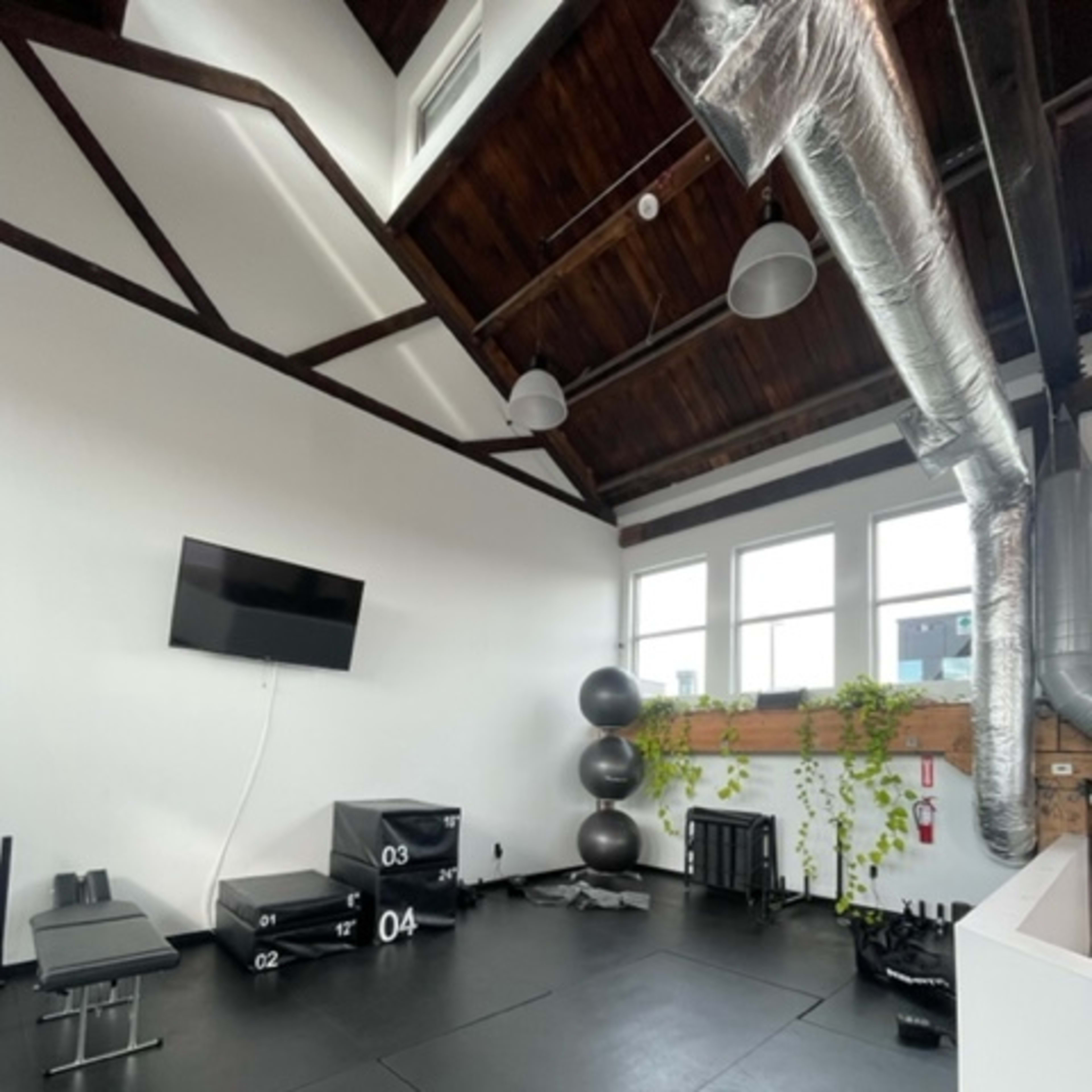 A workout space with black rubber flooring, a wall-mounted television, a weight bench, and various fitness equipment, including exercise boxes and a large stability ball.