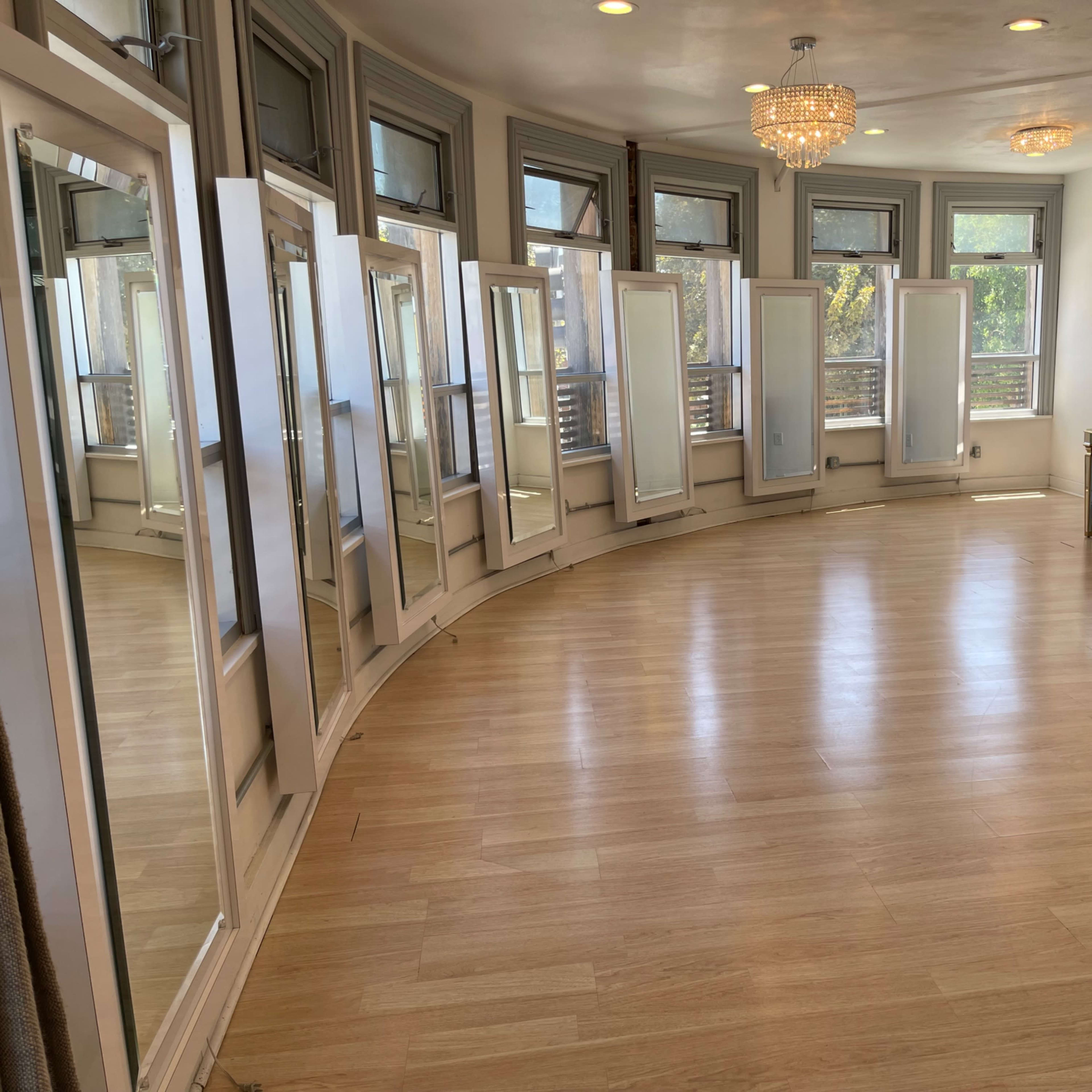 A spacious room with a curved wall of mirrors, hardwood flooring, and a table with two chairs near the windows.