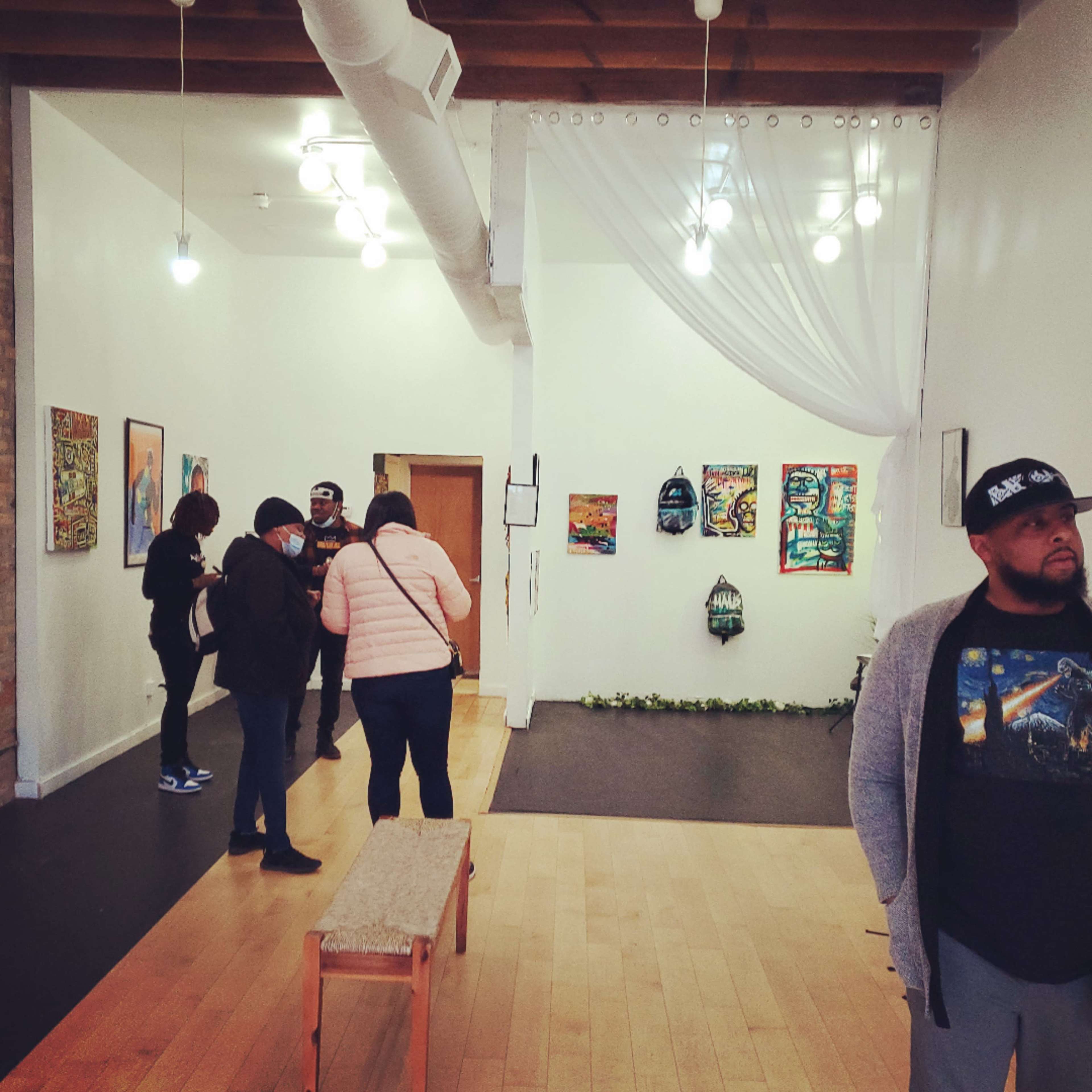 An art gallery with several people browsing the artwork displayed on the walls and a bench in the foreground.