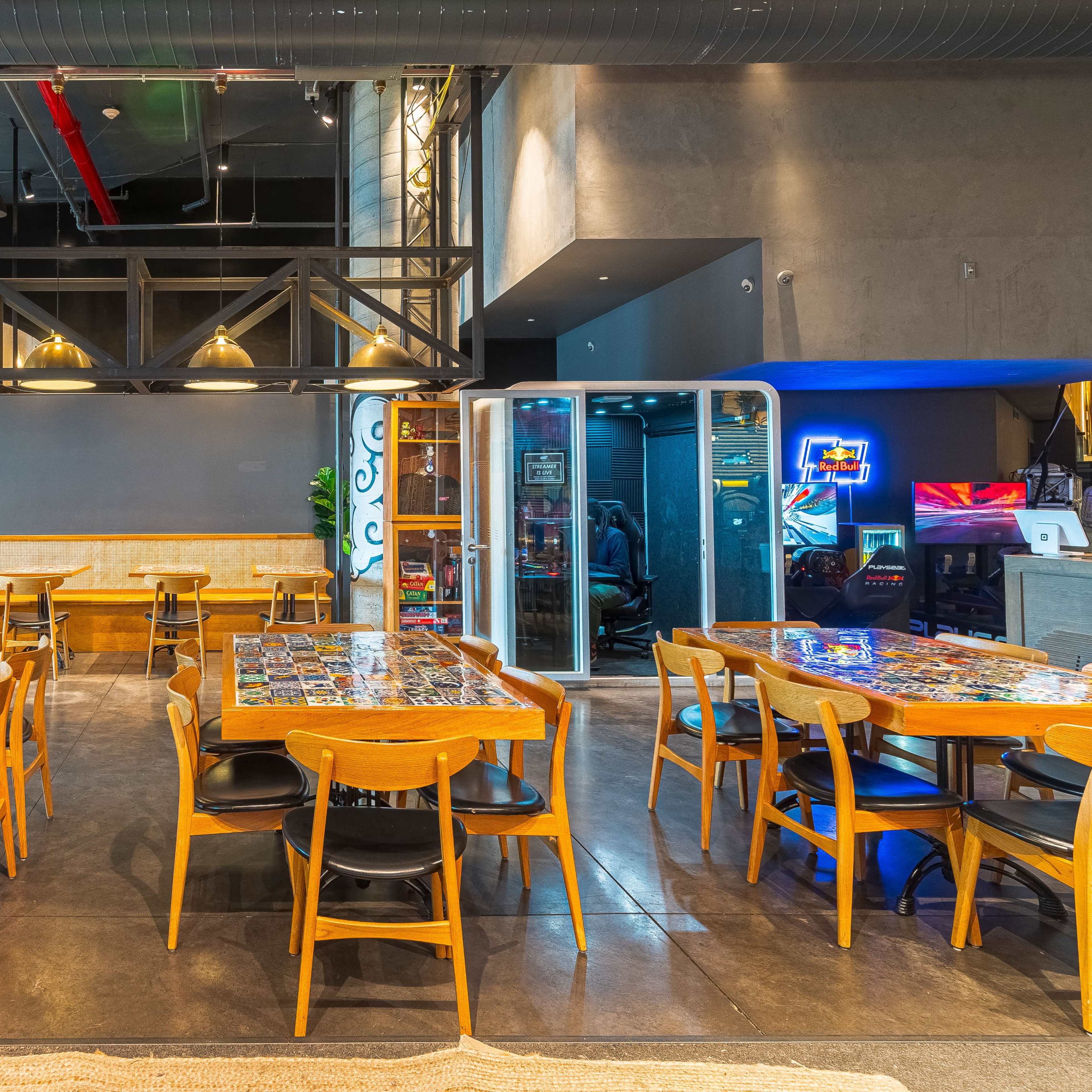 A modern restaurant interior with wooden tables and black chairs arranged in a spacious setting, featuring a mix of vibrant decor and industrial elements.