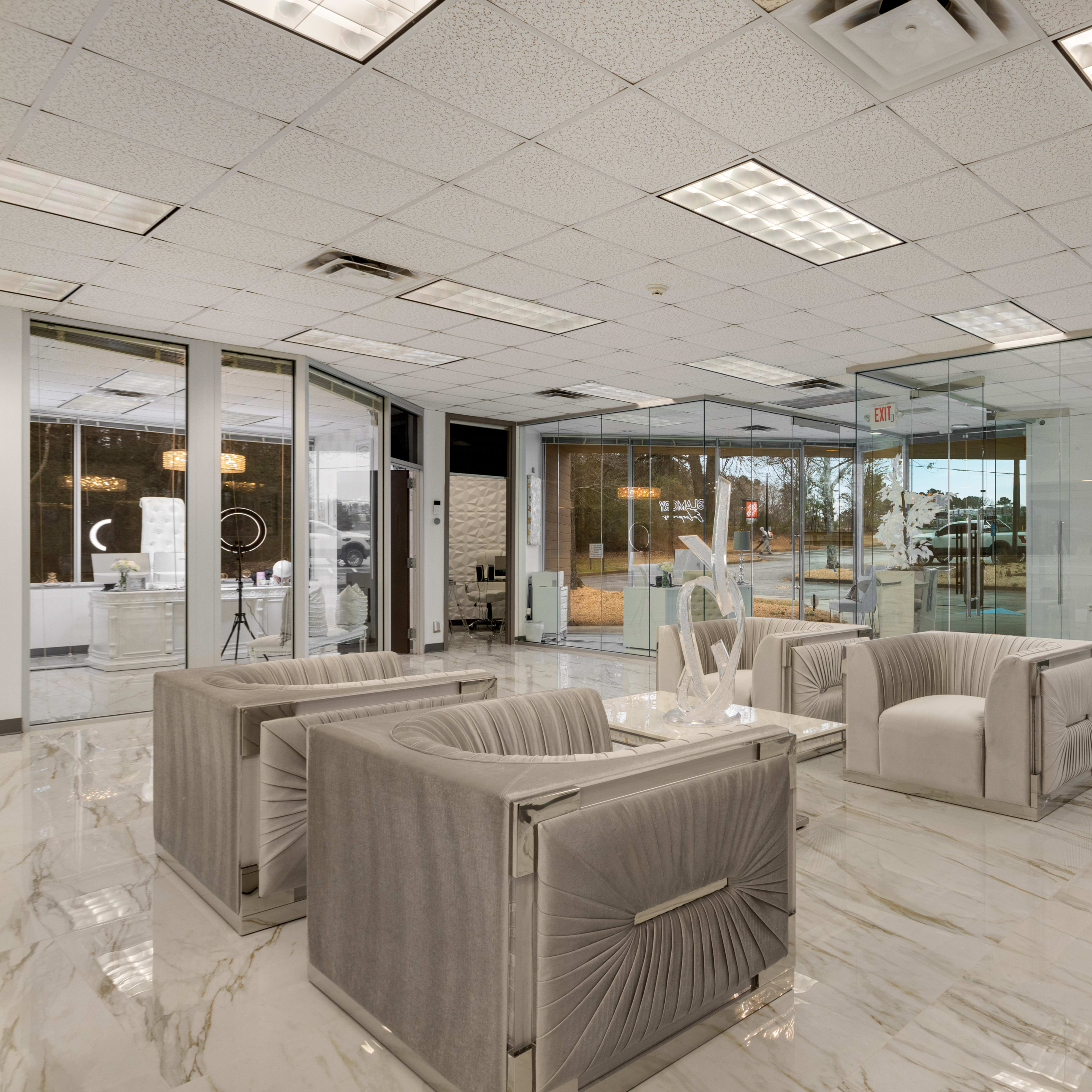 A modern office space with glass walls, marble flooring, and a seating area featuring plush armchairs.