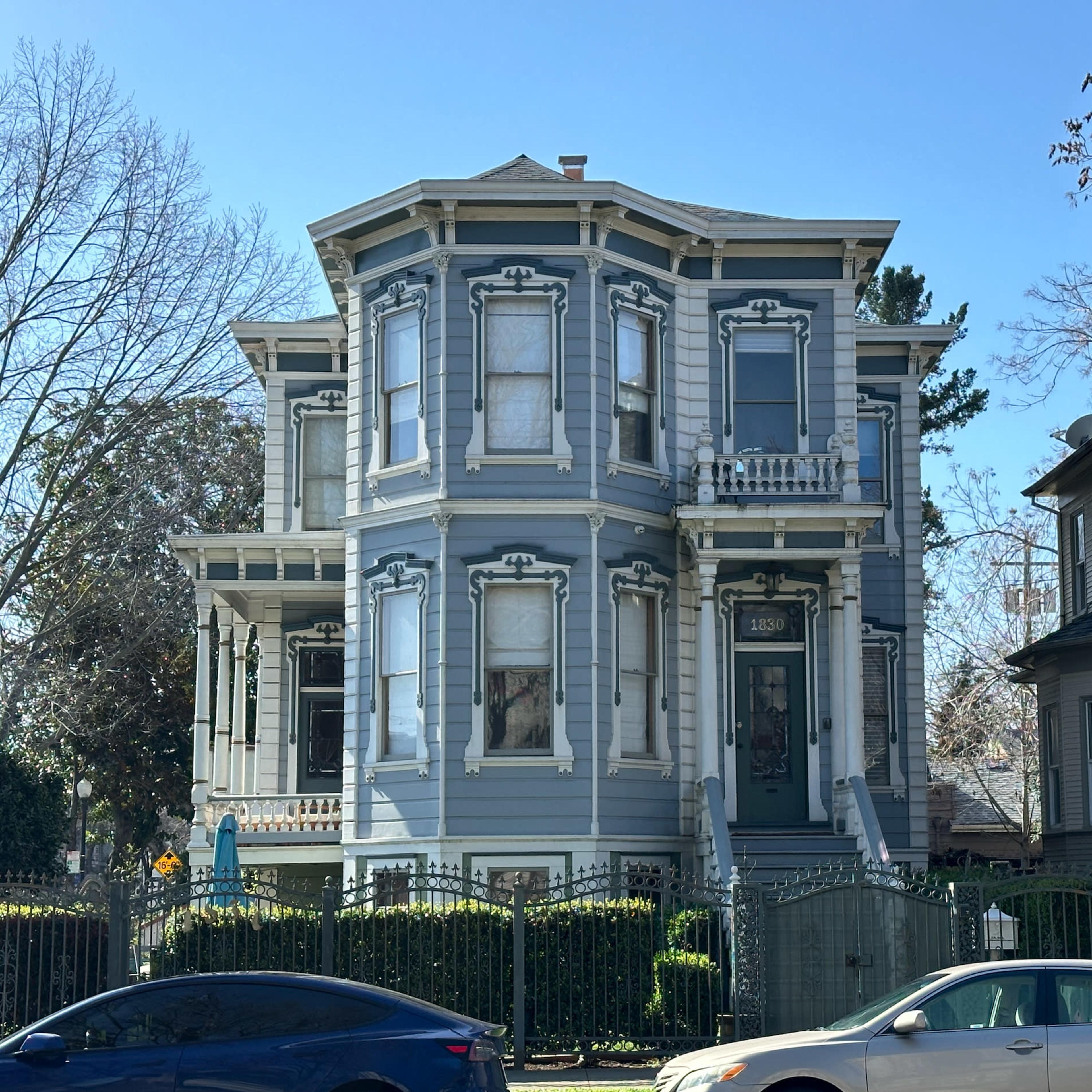 A large Victorian-style house painted blue, featuring intricate architectural details and a fenced yard.