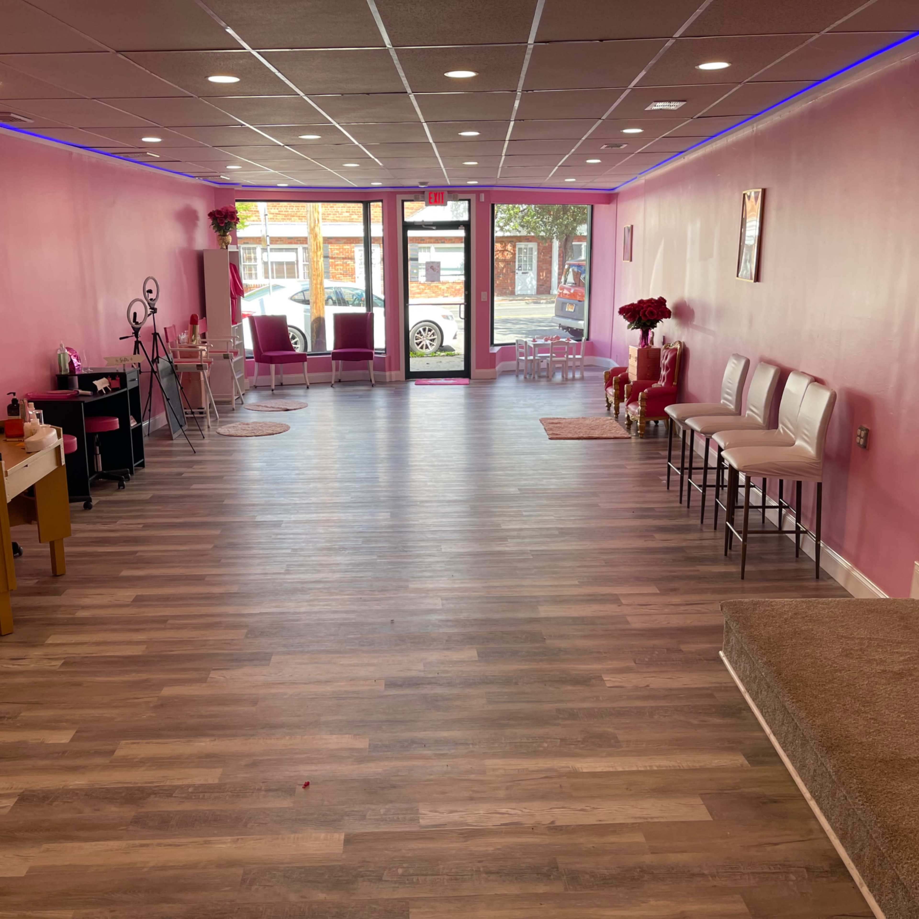 A spacious pink-themed salon interior with wooden flooring, featuring a waiting area with chairs and a reception desk.