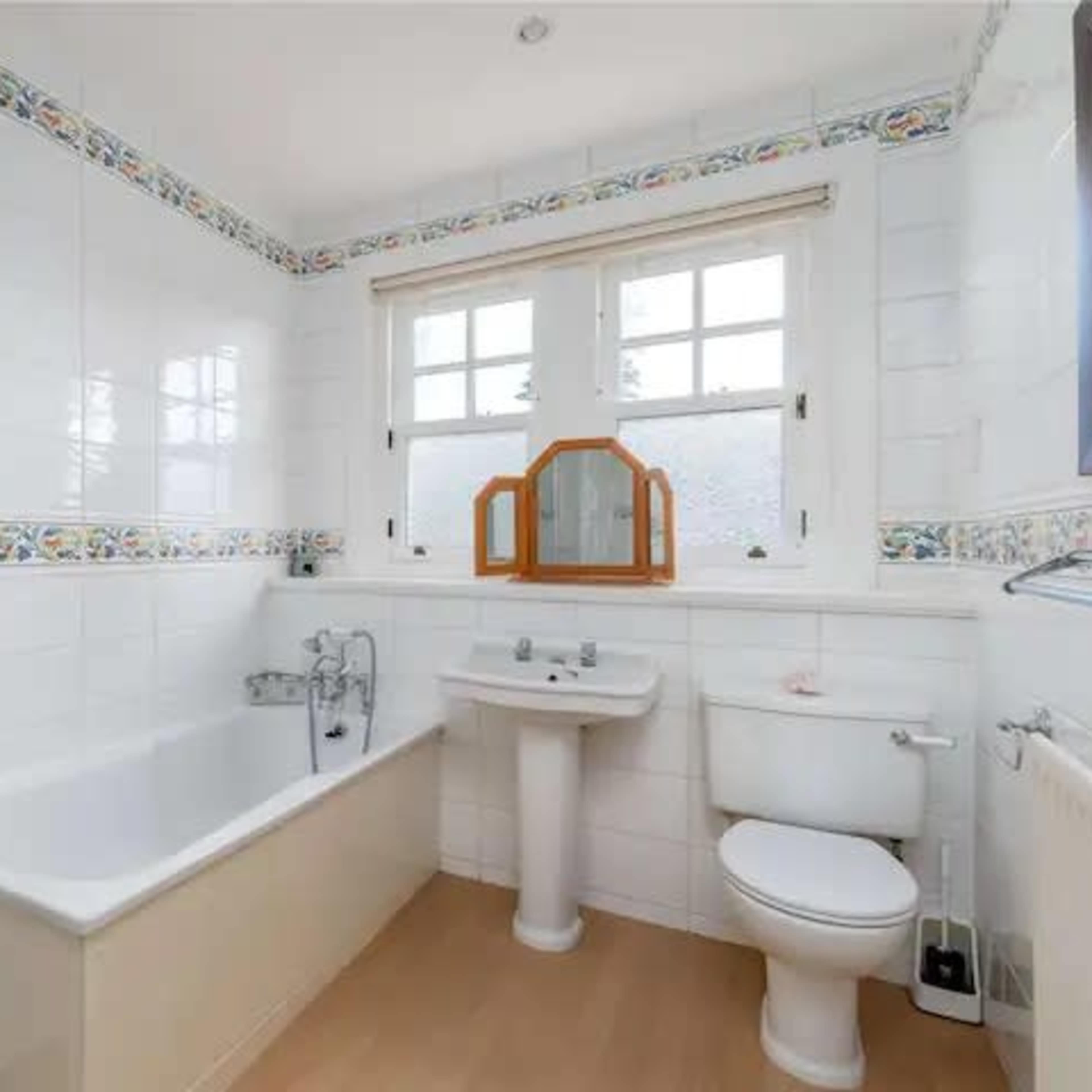 A bathroom with a bathtub, sink, toilet, and decorative tiled border along the walls.