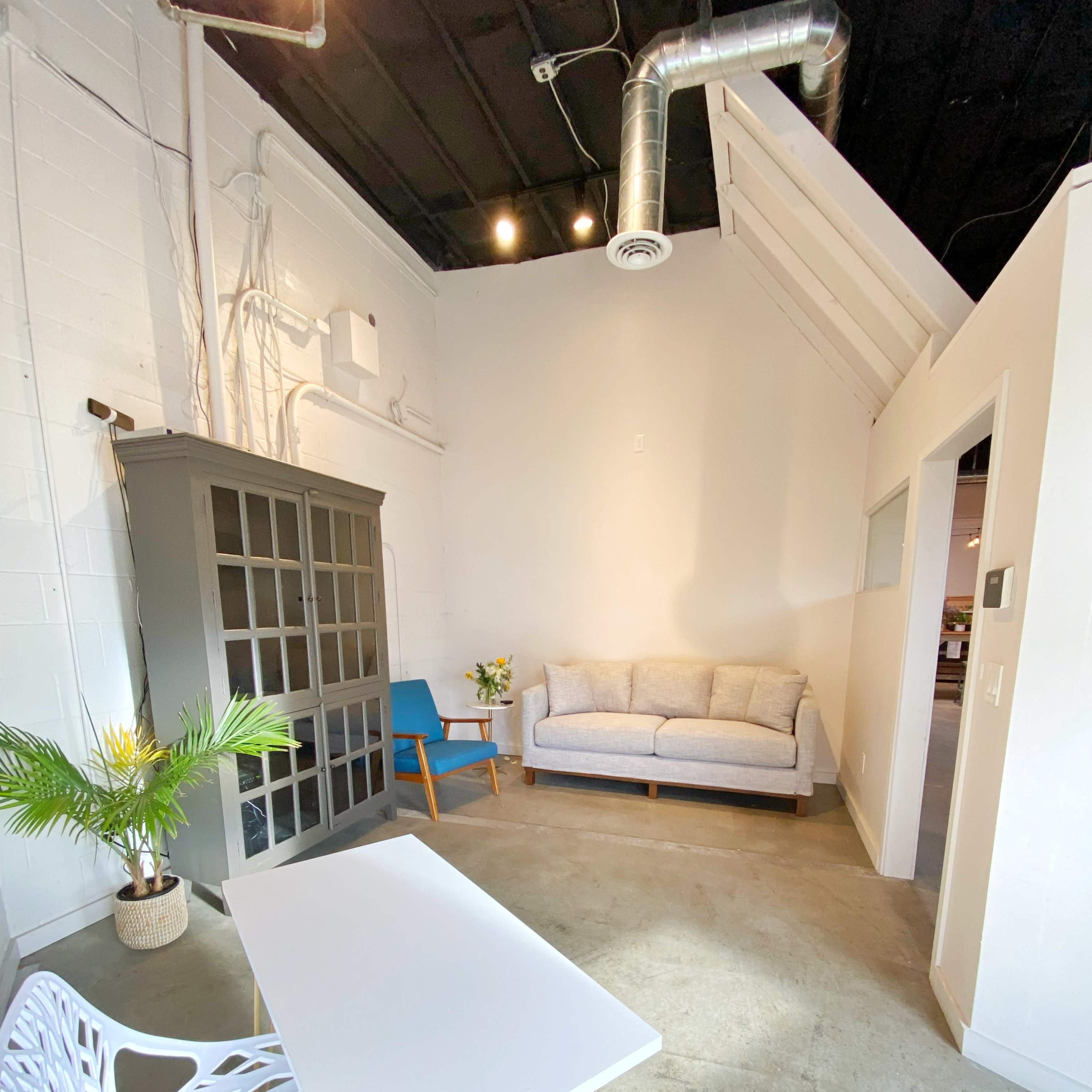 A bright room features a gray couch, a small table with a decorative chair, and a plant, accentuated by industrial-style elements.