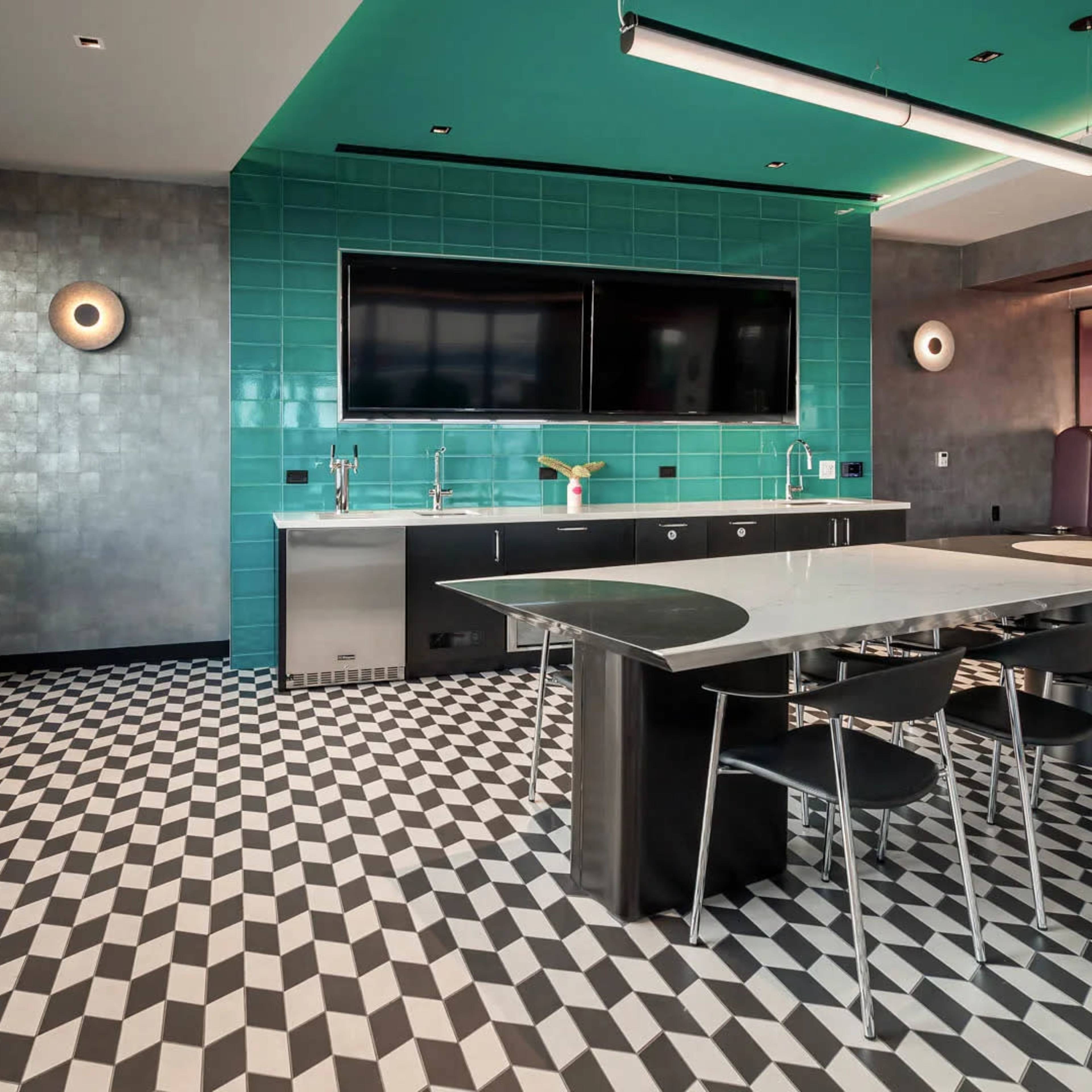 A modern kitchen with teal tiled walls, a large black and white checkerboard floor, a stainless steel countertop, and a seating area with bright green chairs.