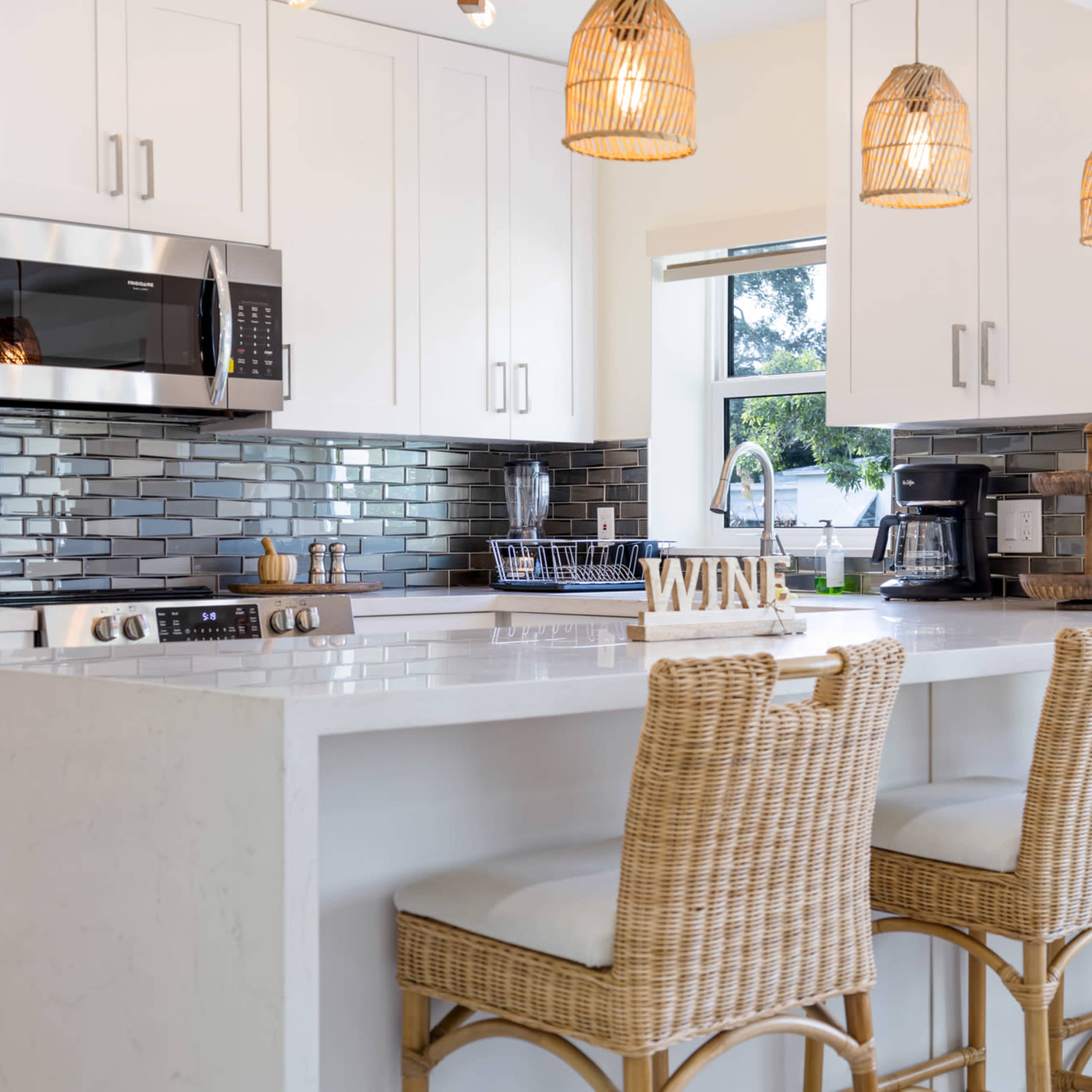 A modern kitchen features a white island with bar stools, pendant lights, and stainless steel appliances.