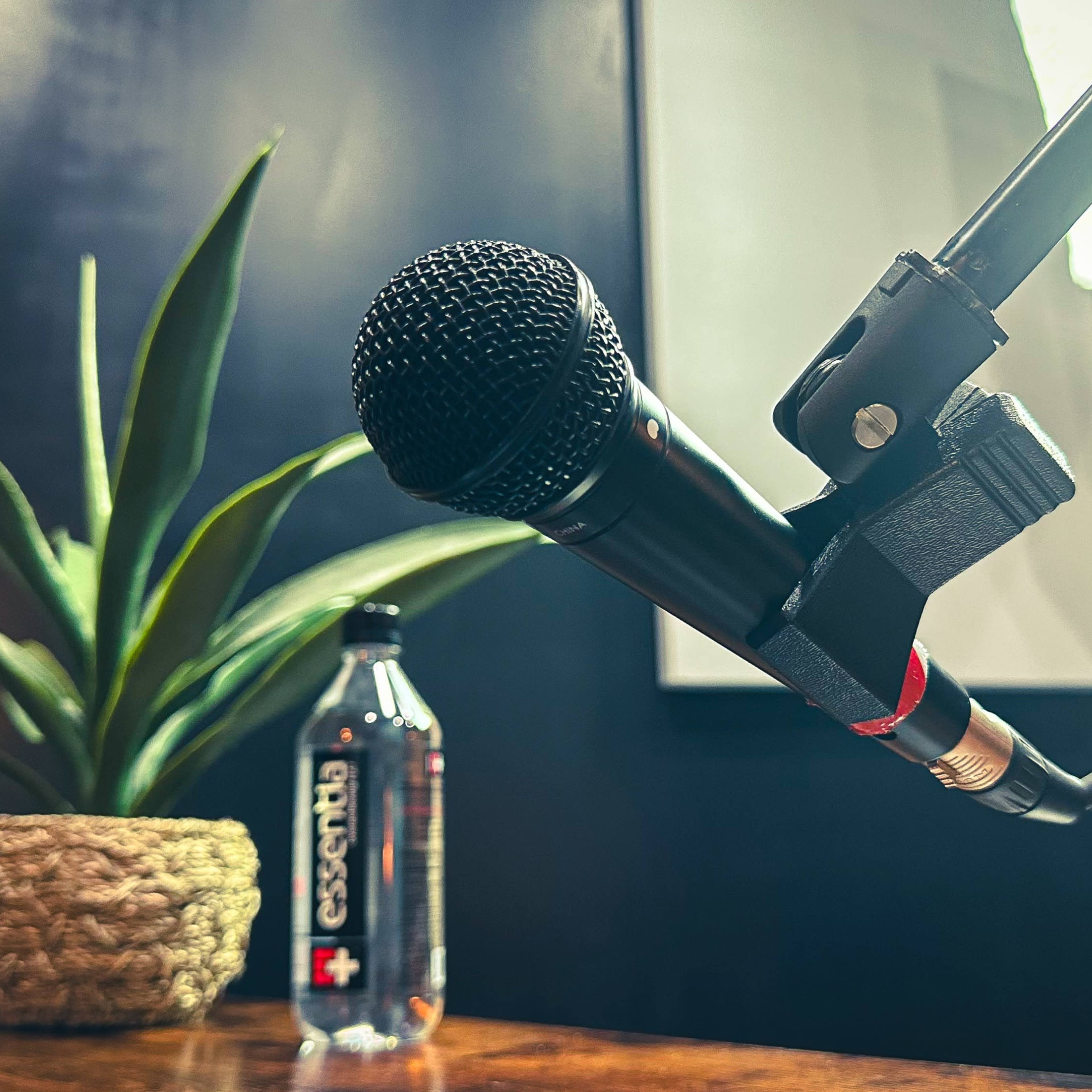 A microphone is positioned in front of a potted plant and a bottle of water on a wooden table.