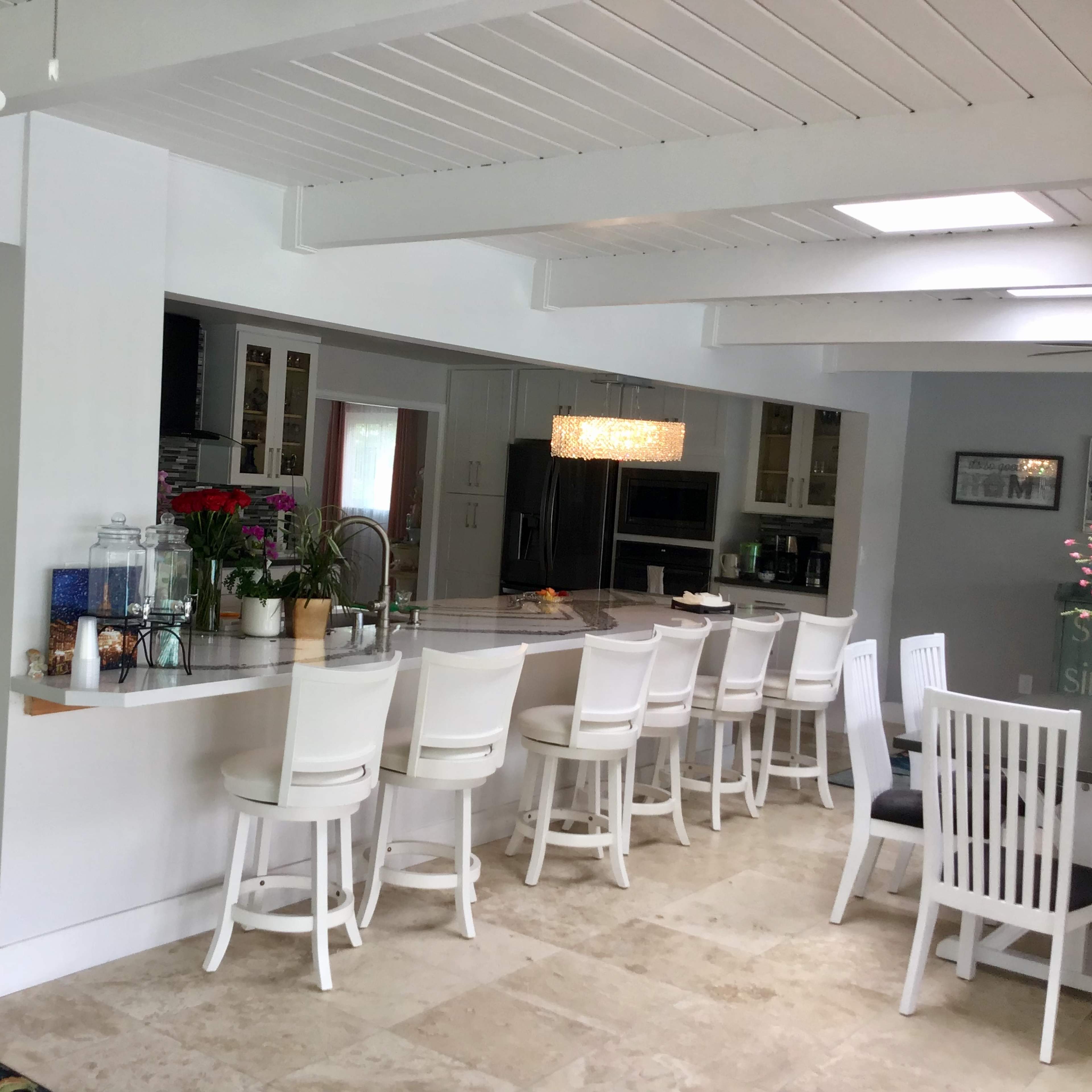 A modern kitchen with a long, white countertop and several white barstools arranged along one side.