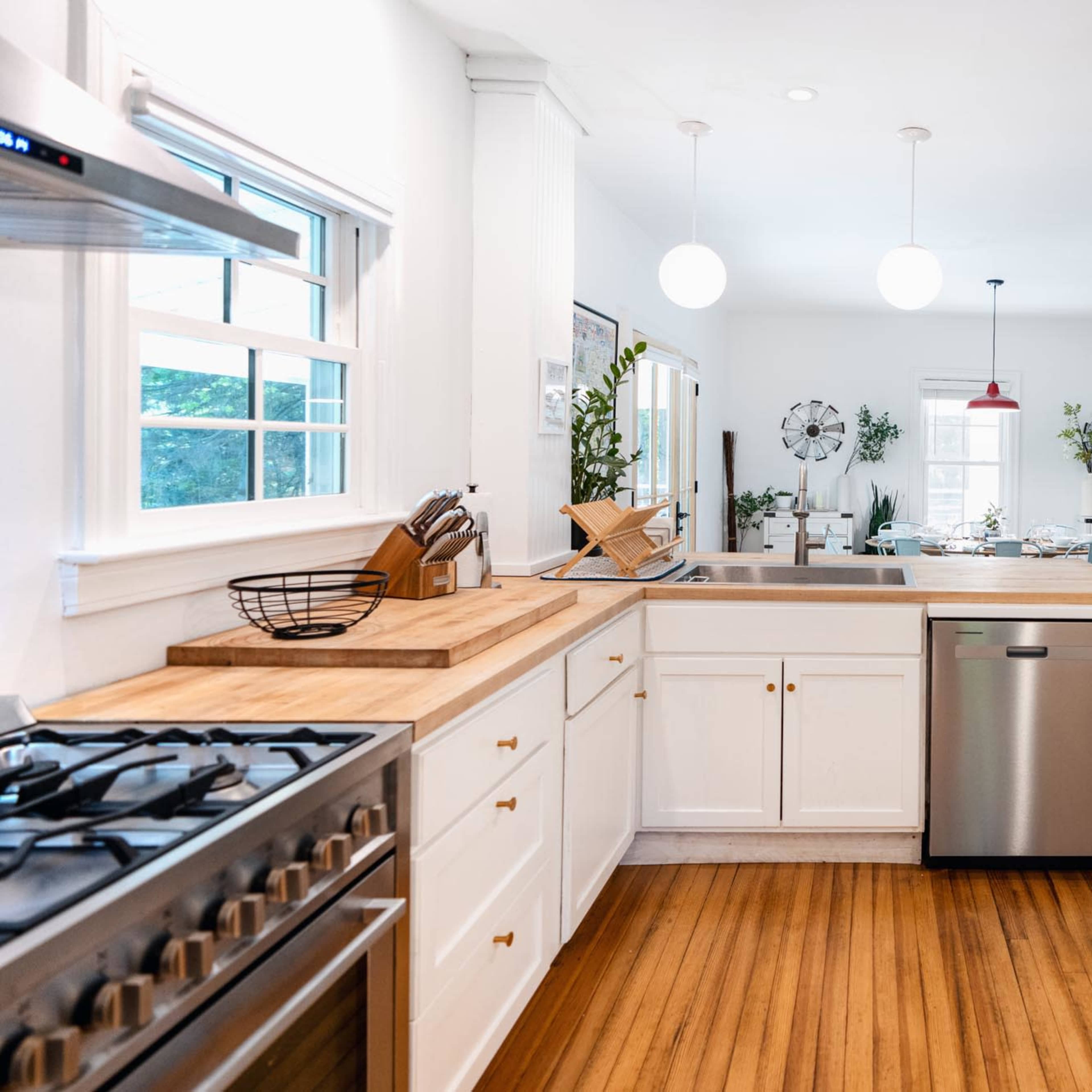 A bright kitchen features a central island with a wooden countertop, stainless steel appliances, and a view of a dining area in the background.