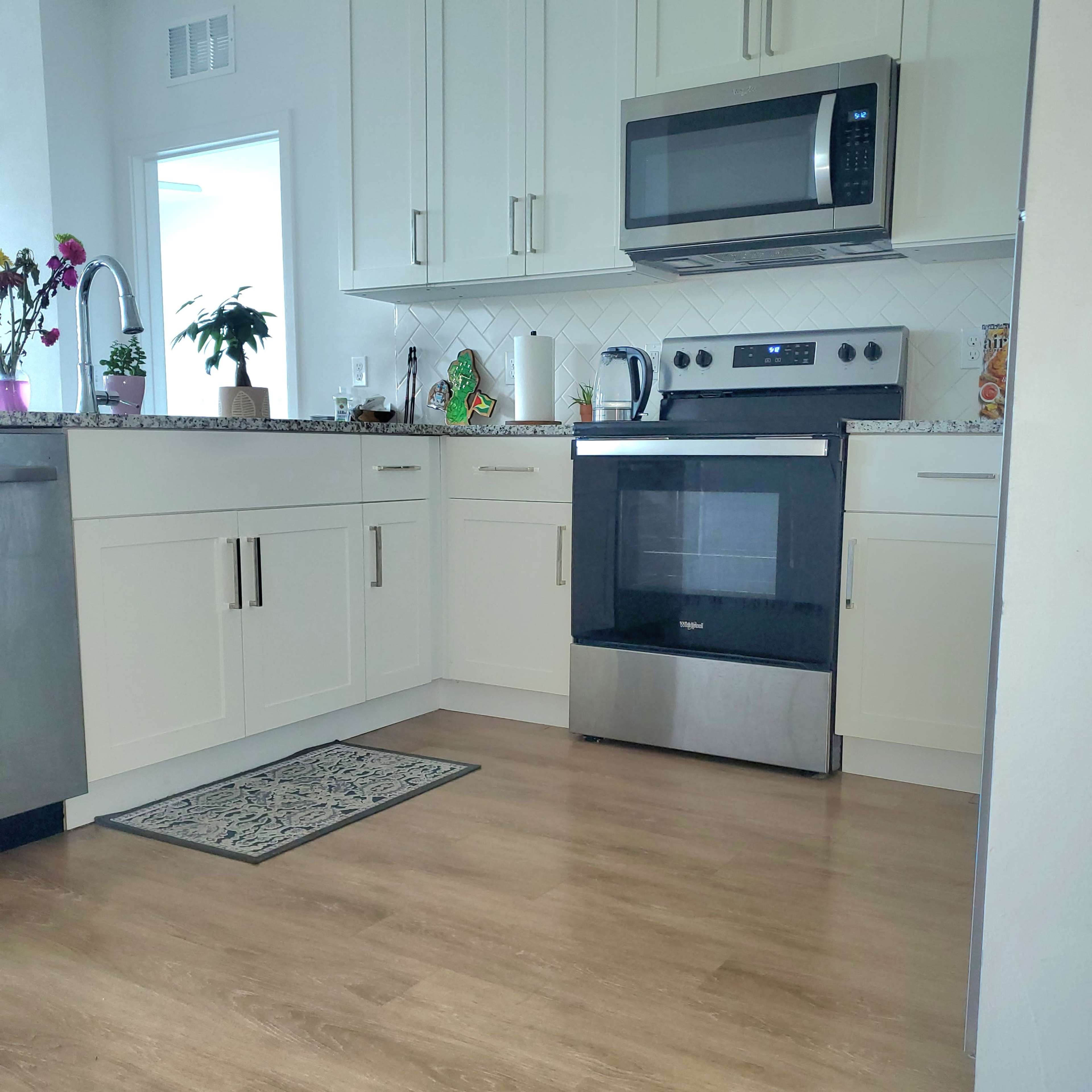 A modern kitchen with white cabinets, a stainless steel microwave above an oven, and a patterned rug on the wooden floor.