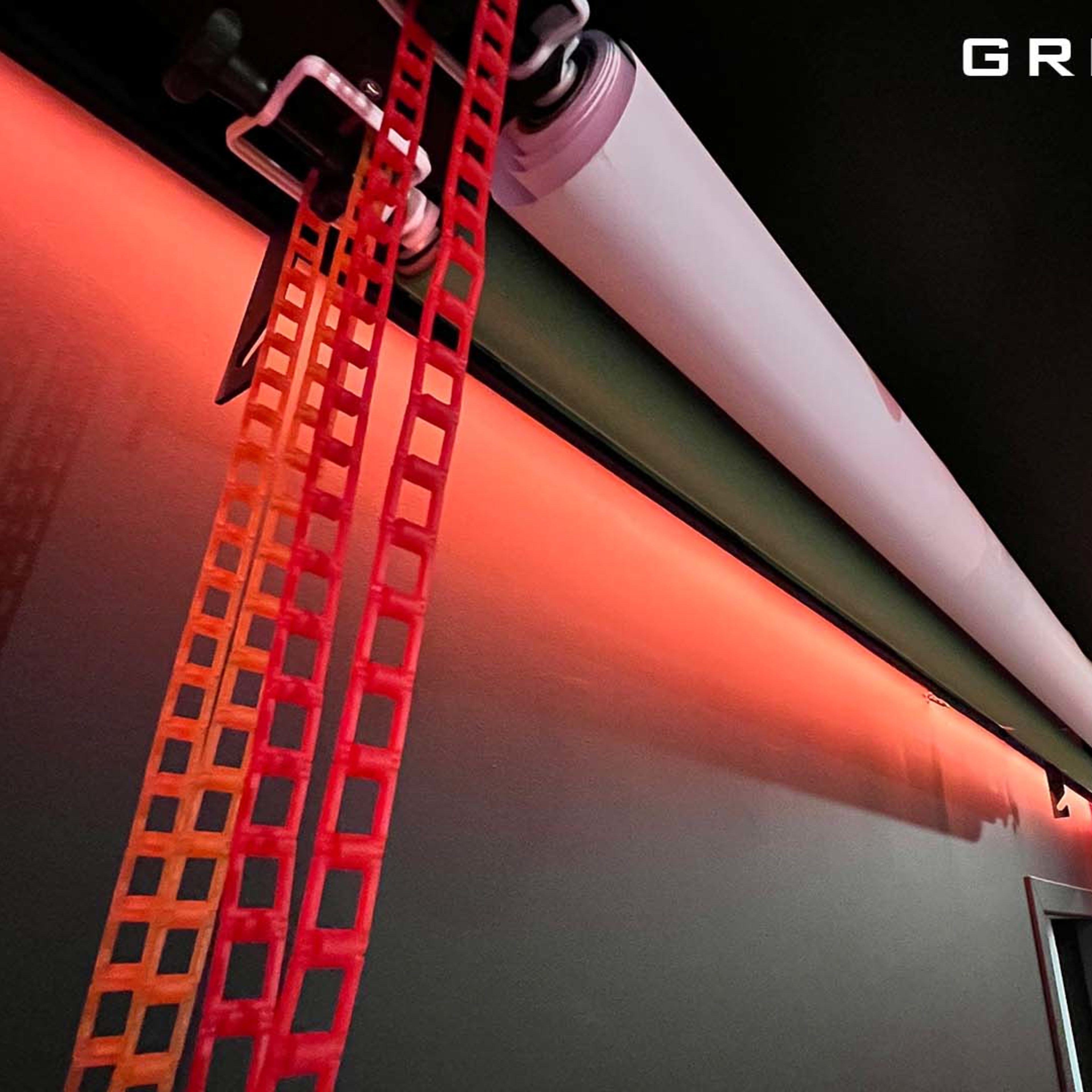 A ceiling-mounted green screen roll with a red and black strip along the side and overhead lighting illuminating the space.