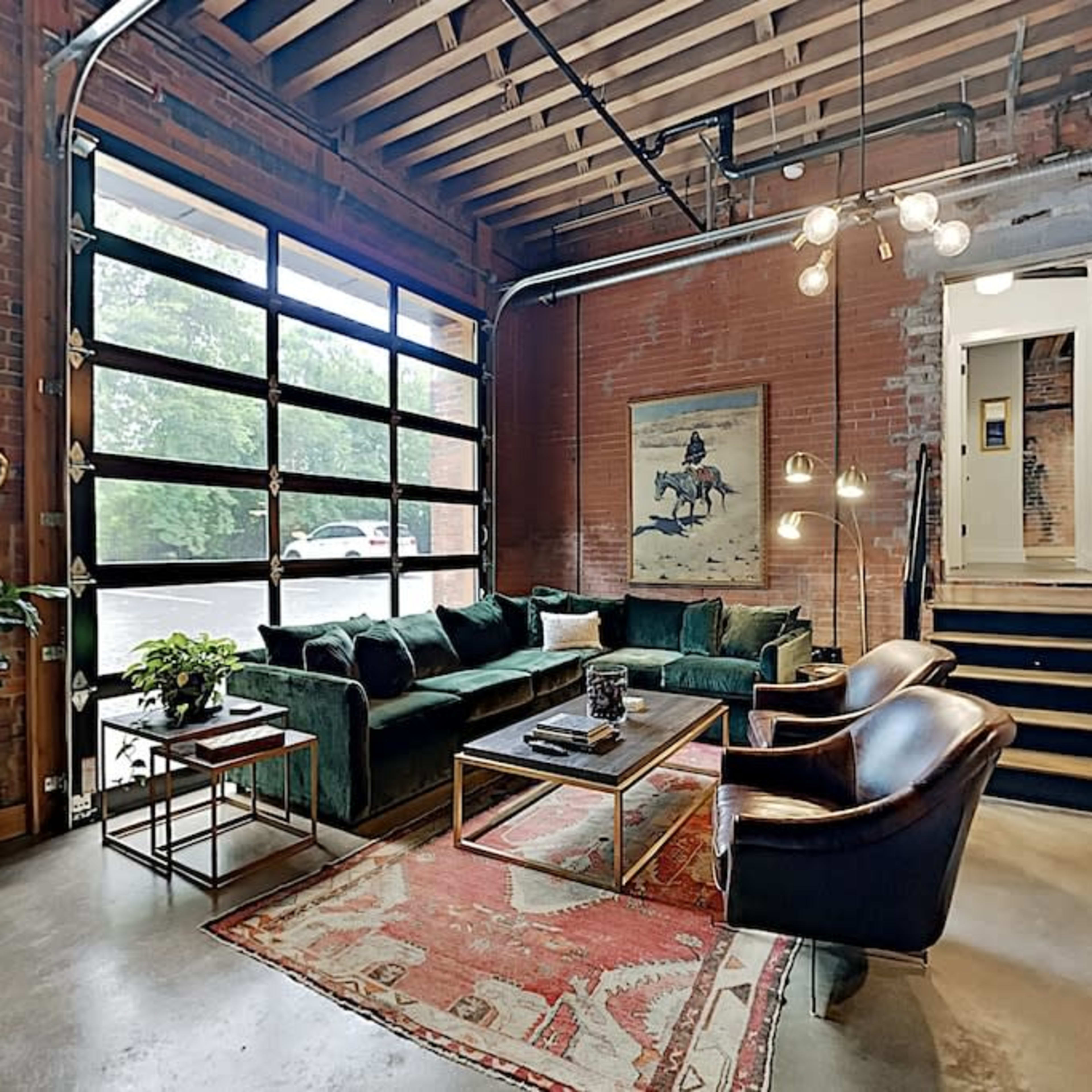 A modern living room with a green velvet sofa, a wooden coffee table, and an open garage-style door that allows natural light into the space.