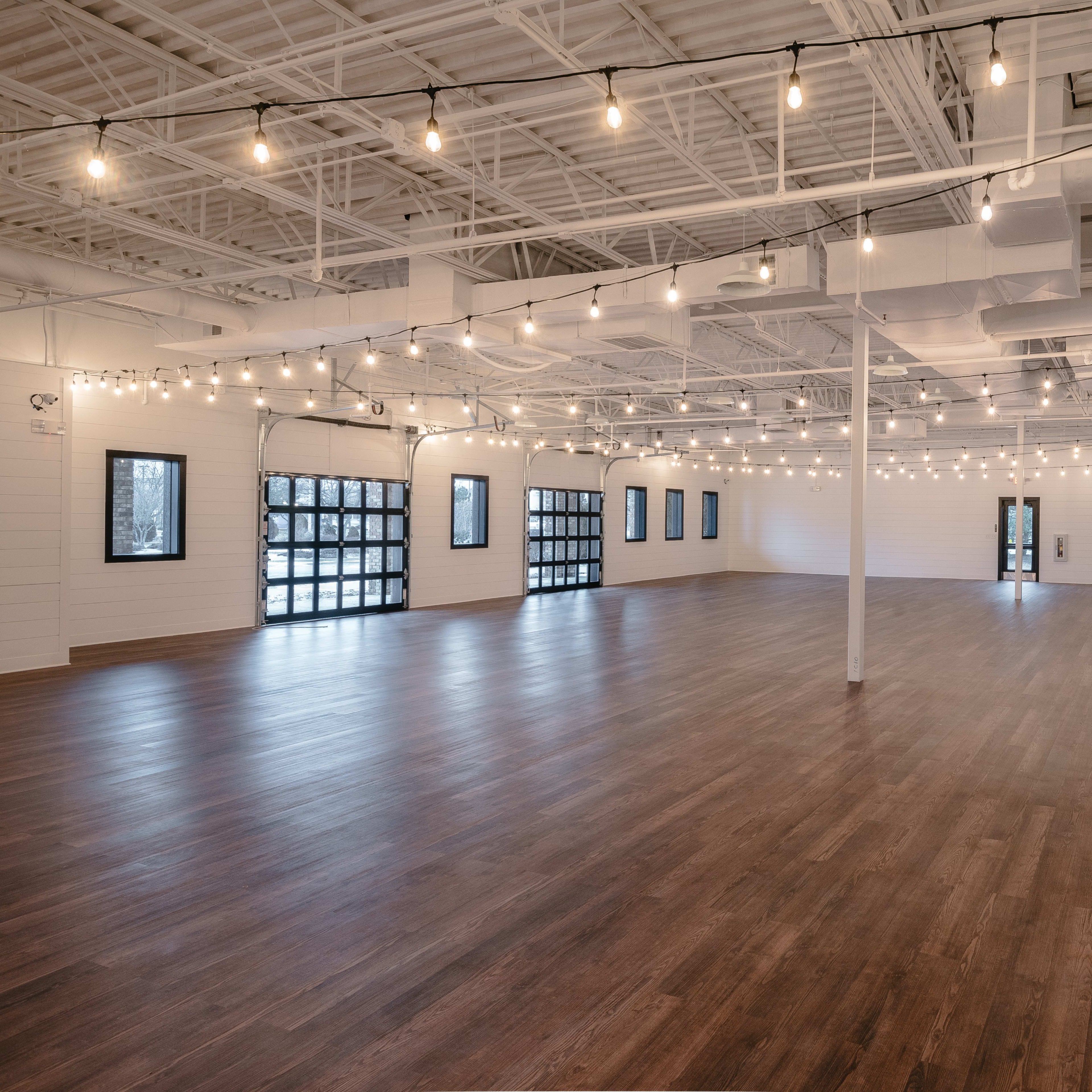 A spacious, empty room with wooden floors and string lights hanging from the ceiling.