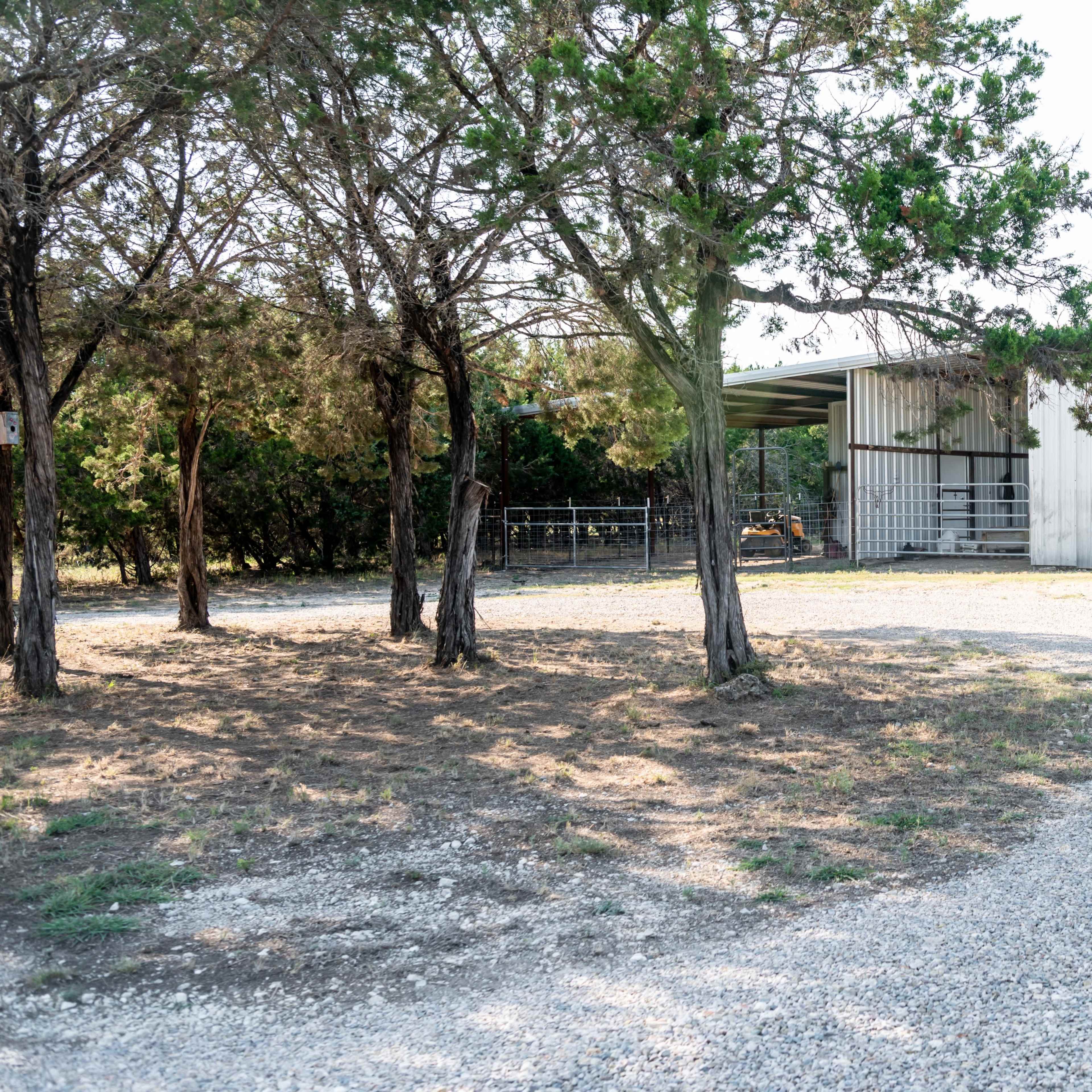 A gravel path leads to a metal structure surrounded by trees on a rural property.