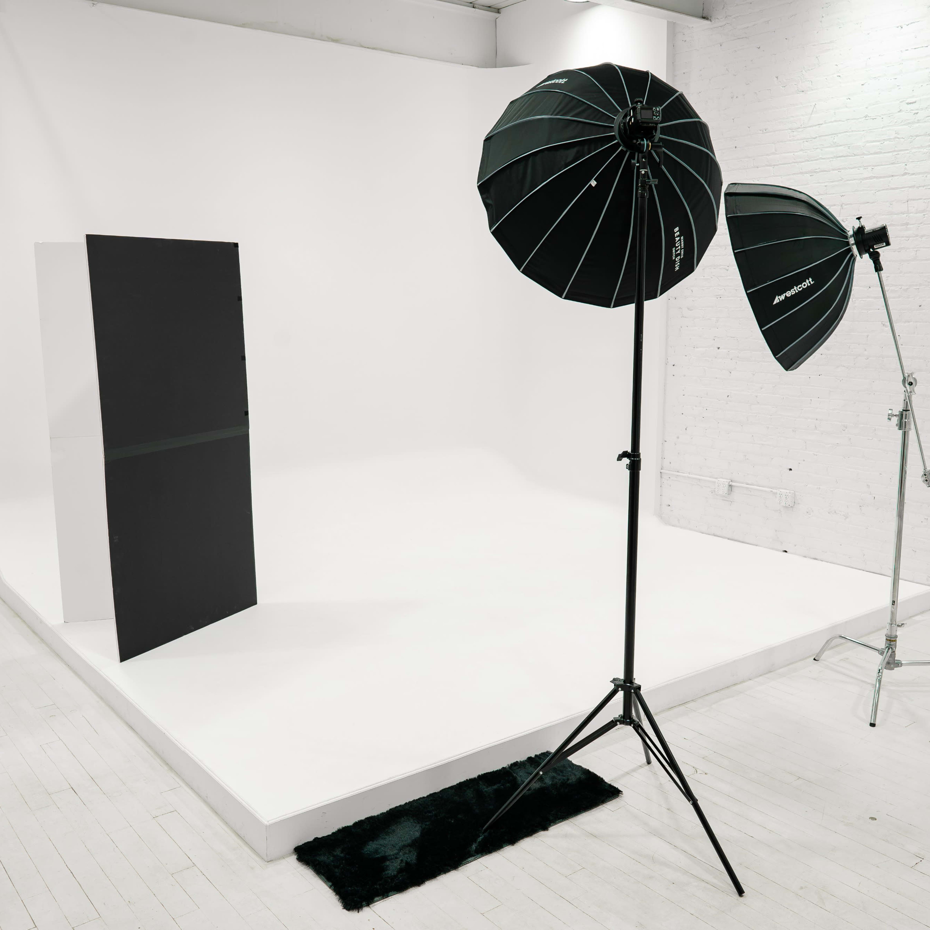 A photography studio with a white backdrop, two light stands with softboxes, and a black fabric divider on the set.