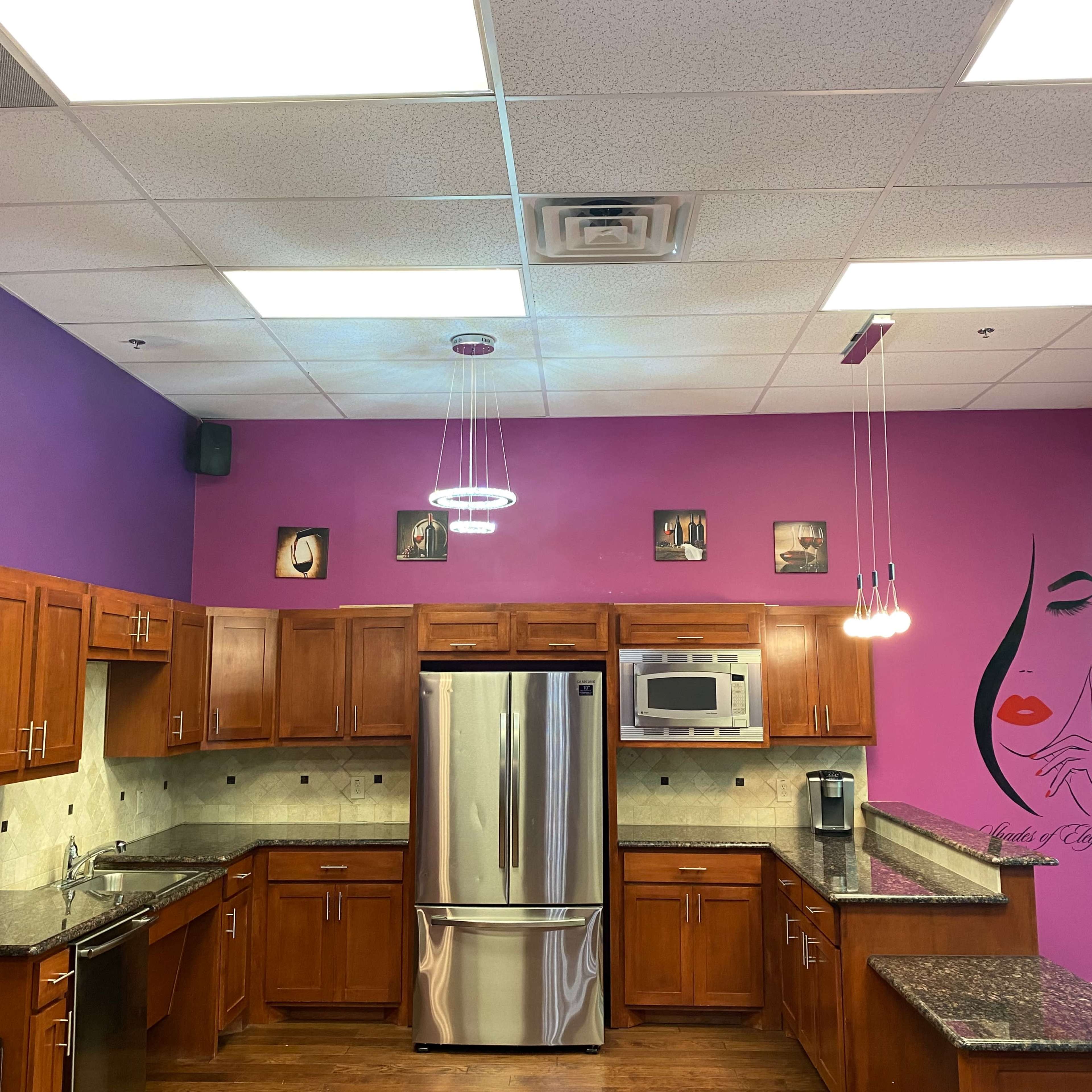 A kitchen with wooden cabinets, gray countertops, and purple walls adorned with art and lighting fixtures.