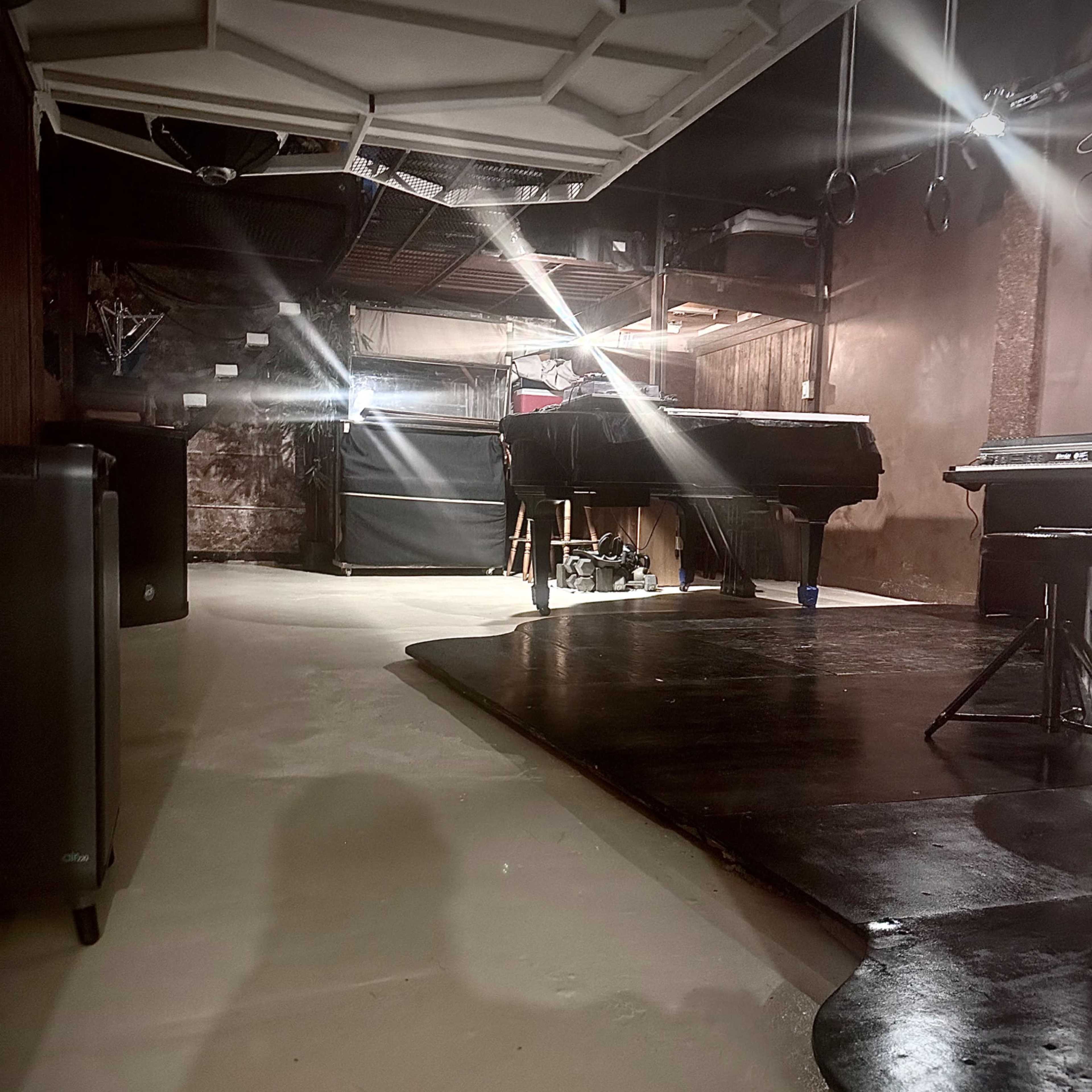 A dimly lit basement space with a smooth floor, dark furniture, and a variety of equipment arranged throughout the area.