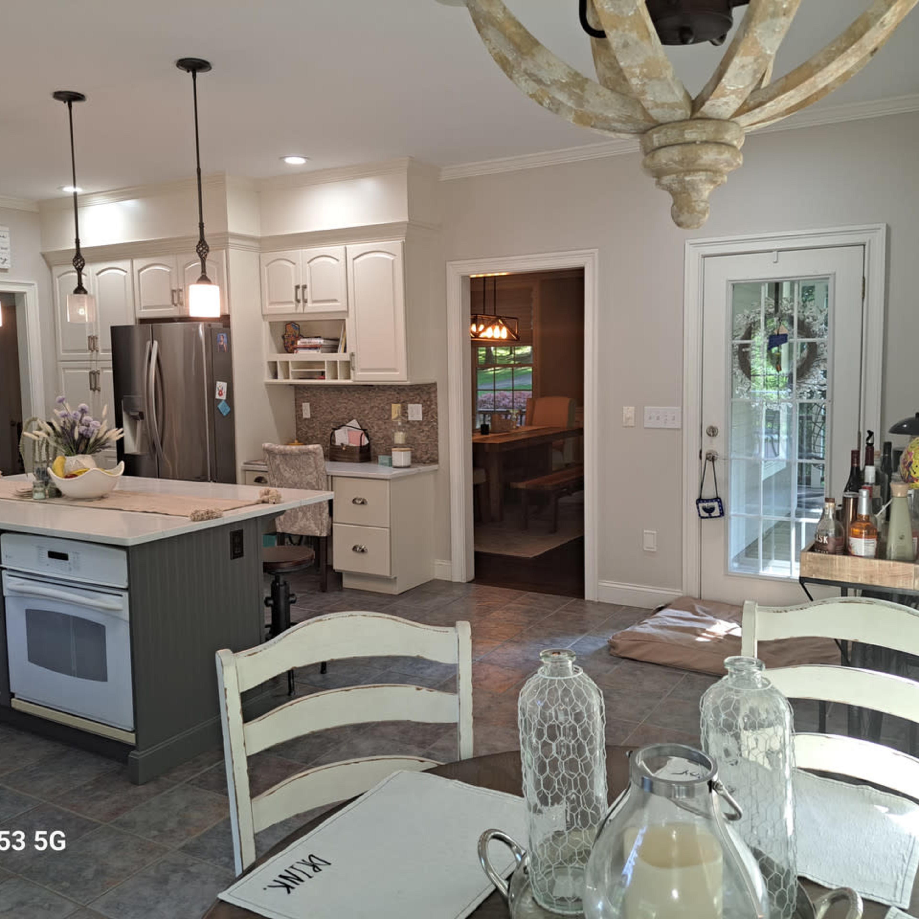 A modern kitchen features an island with a stovetop, stainless steel appliances, white cabinetry, and a dining area in the background.