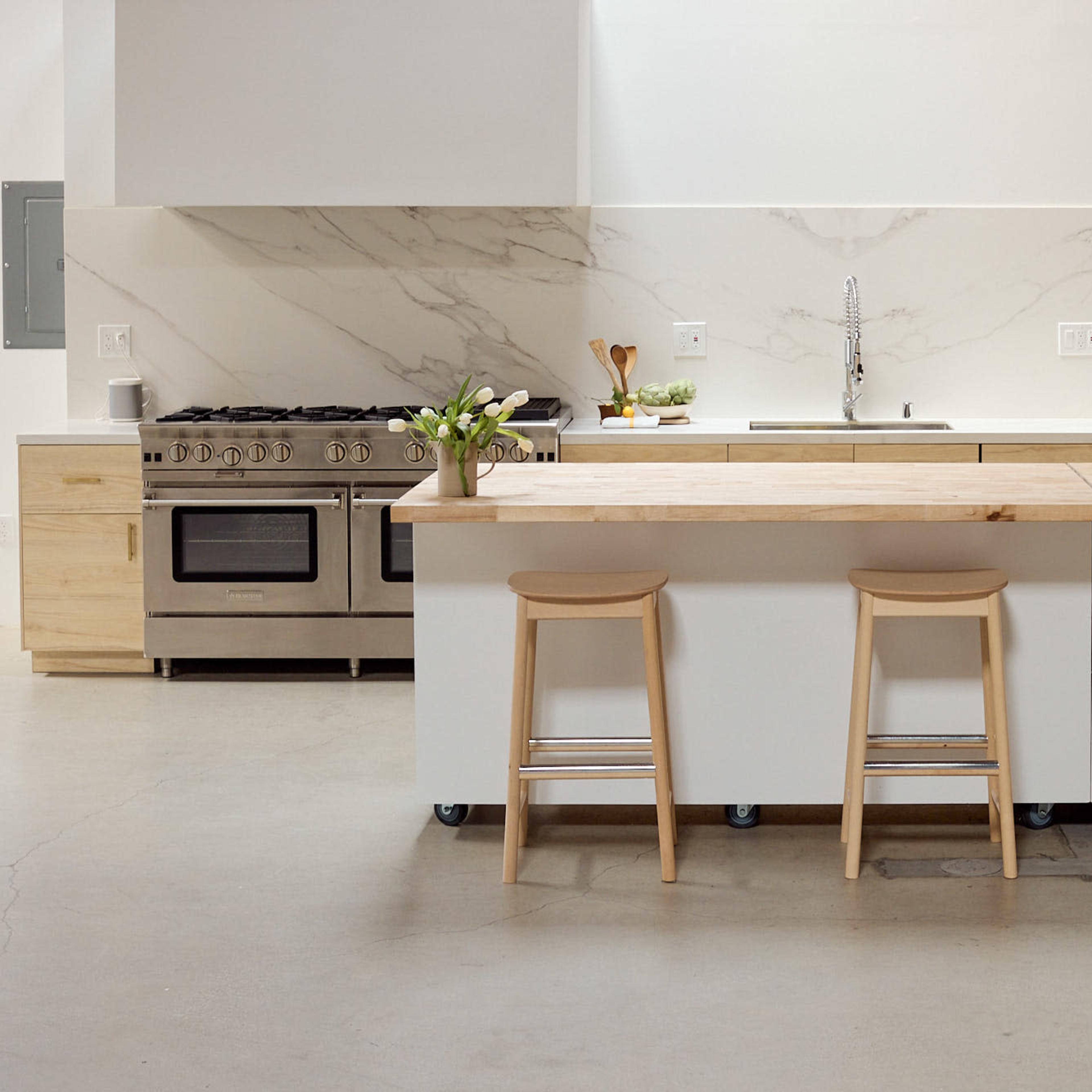 A modern kitchen features a wooden island with stools, stainless steel appliances, and a marble backsplash.