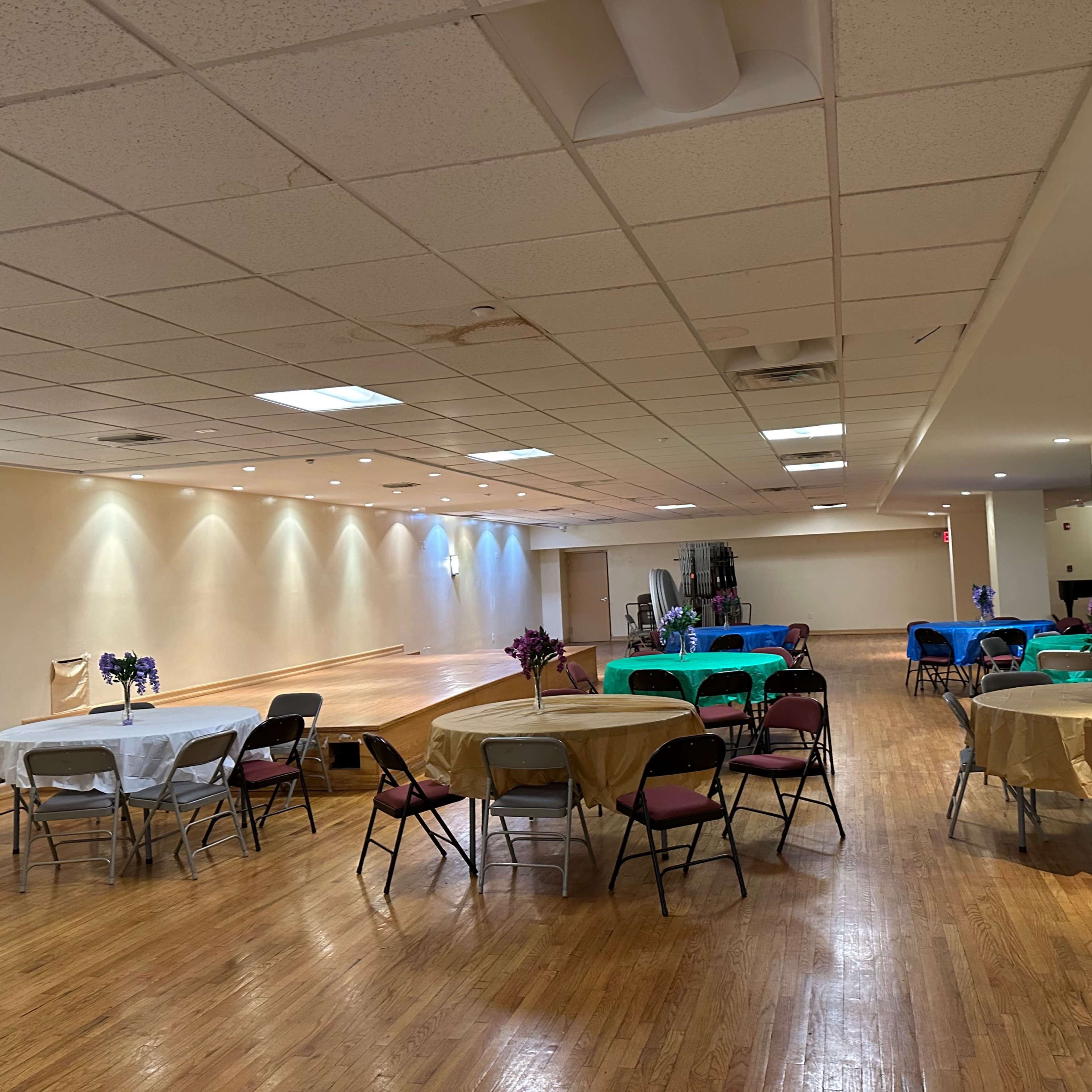 An indoor event space with several round tables set up, each decorated with tablecloths and floral arrangements.