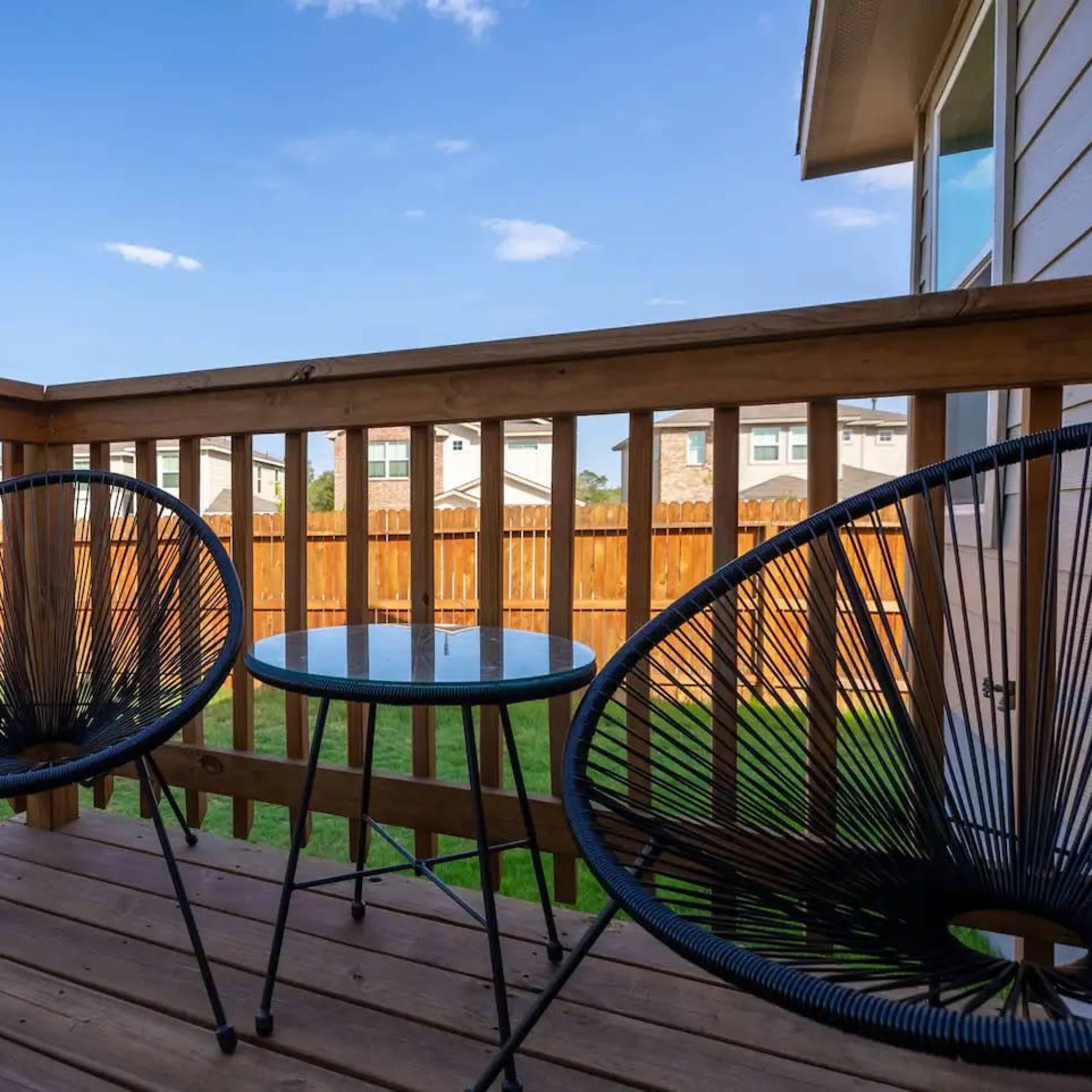 A wooden deck with two black chairs and a small table, overlooking a grassy yard enclosed by a wooden fence.