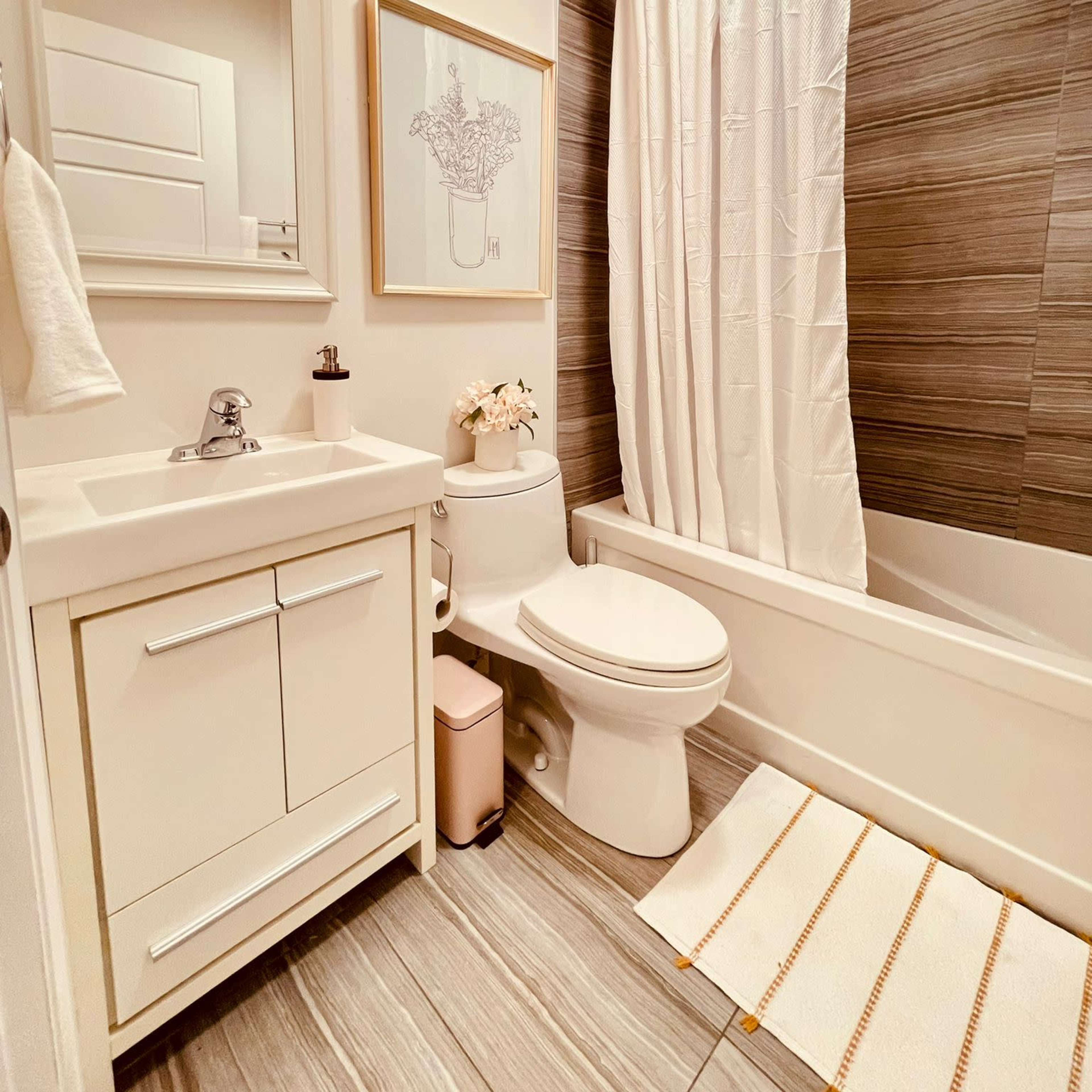 A bathroom featuring a shower-tub combination, a white vanity with a sink, a toilet, and a floral print on the wall.