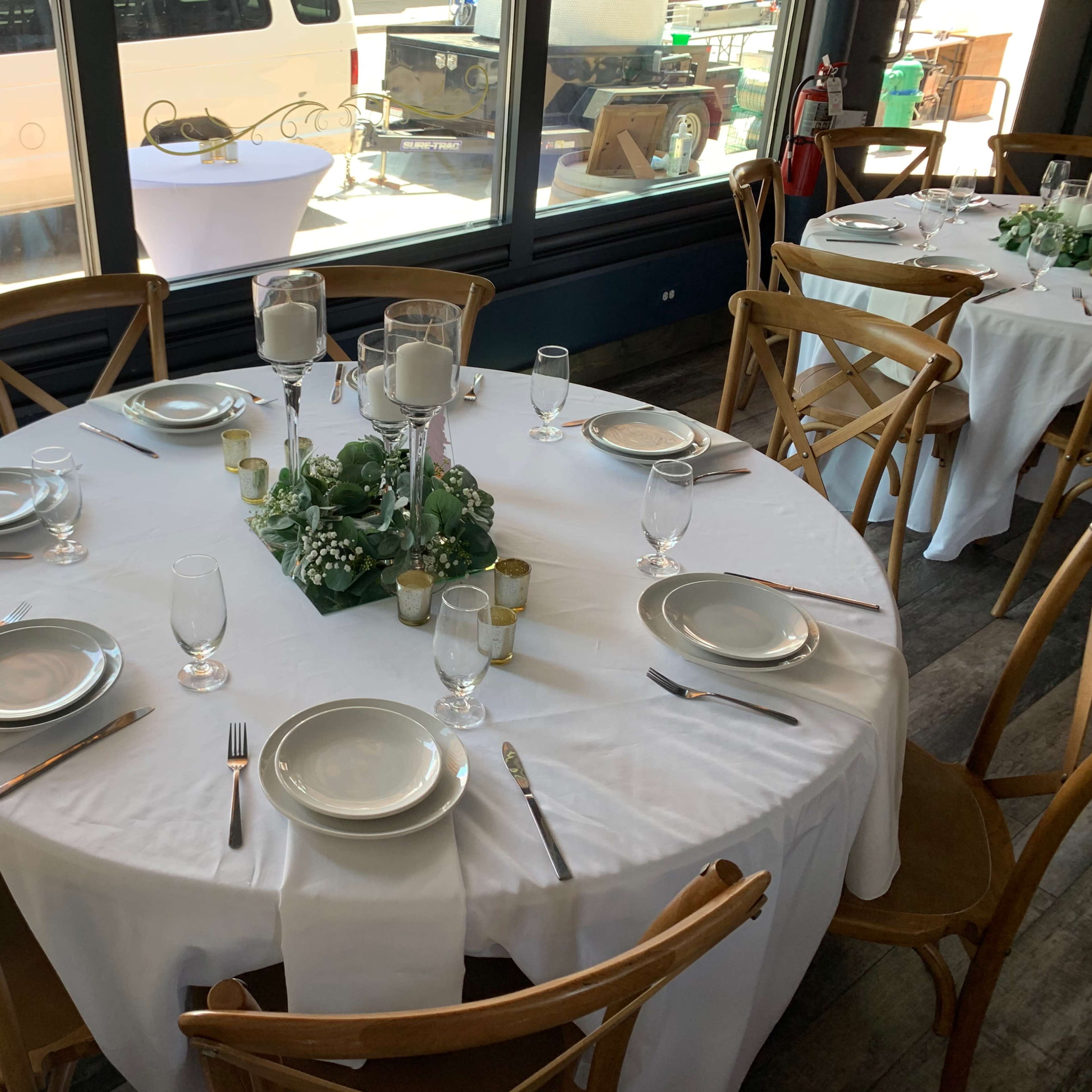A round dining table is set with six place settings, complete with plates, glasses, and utensils, centered with a floral arrangement and candles.