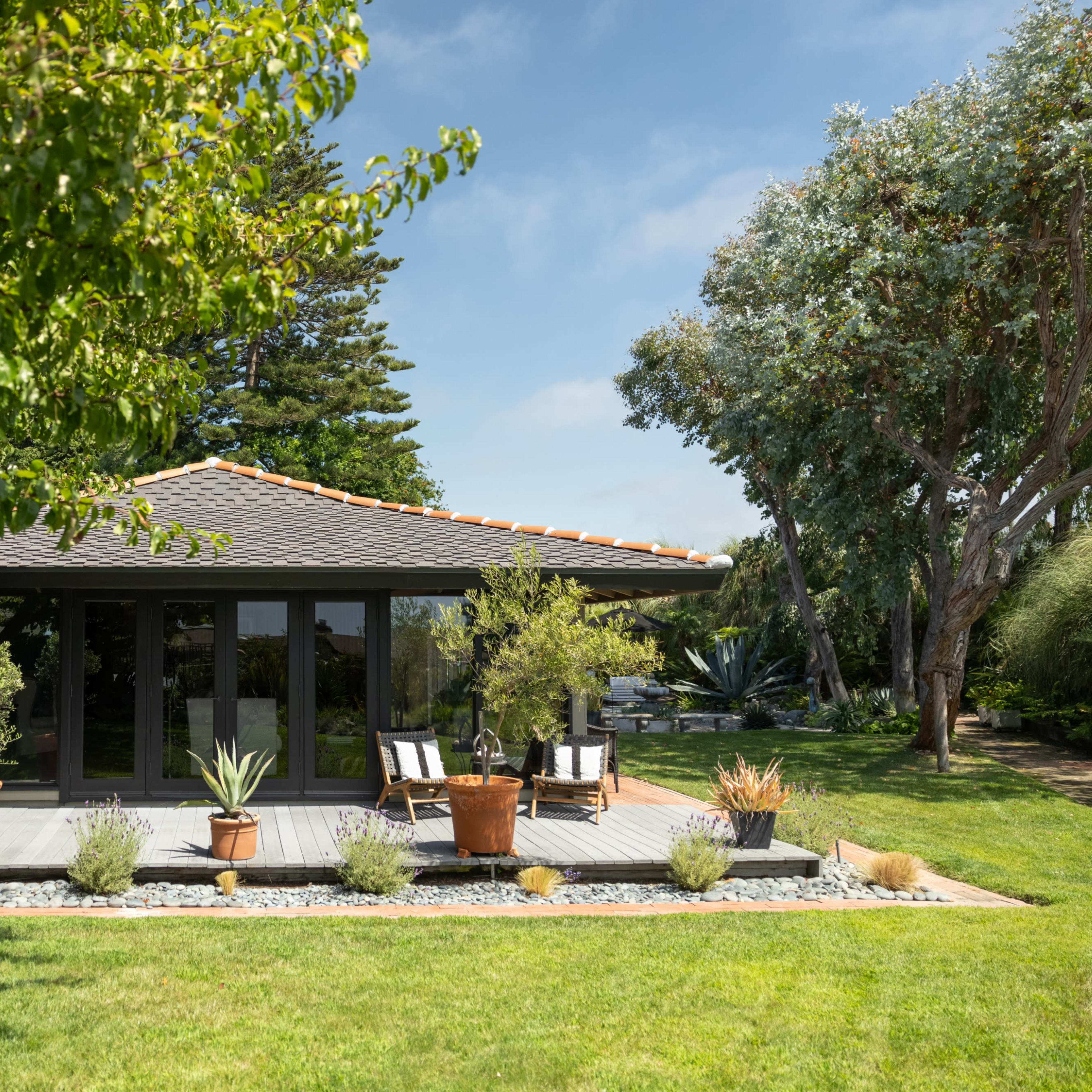 A modern house with a patio is surrounded by a well-maintained garden featuring various plants and trees.
