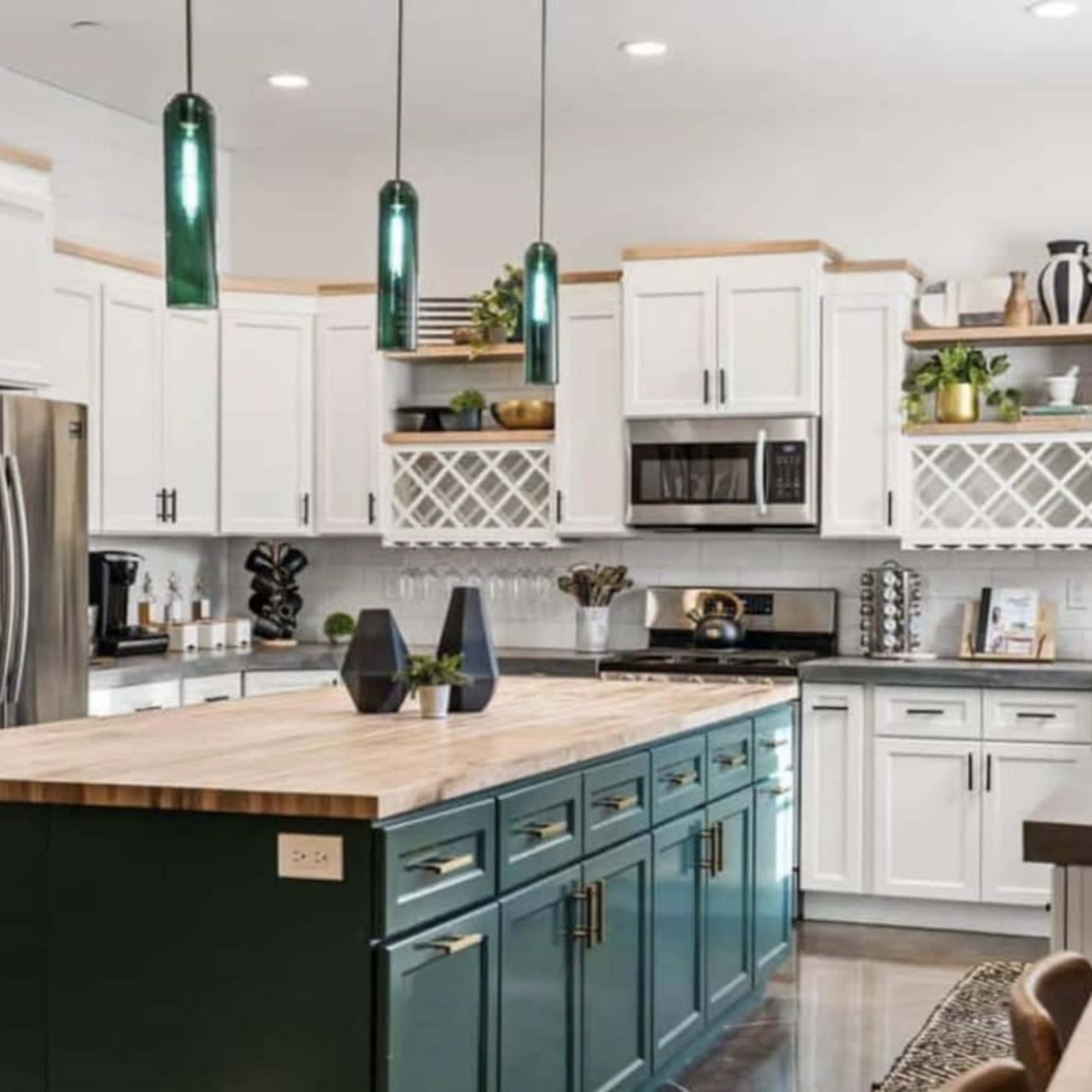 A modern kitchen featuring white cabinetry, a dark green island, stainless steel appliances, and pendant lighting.