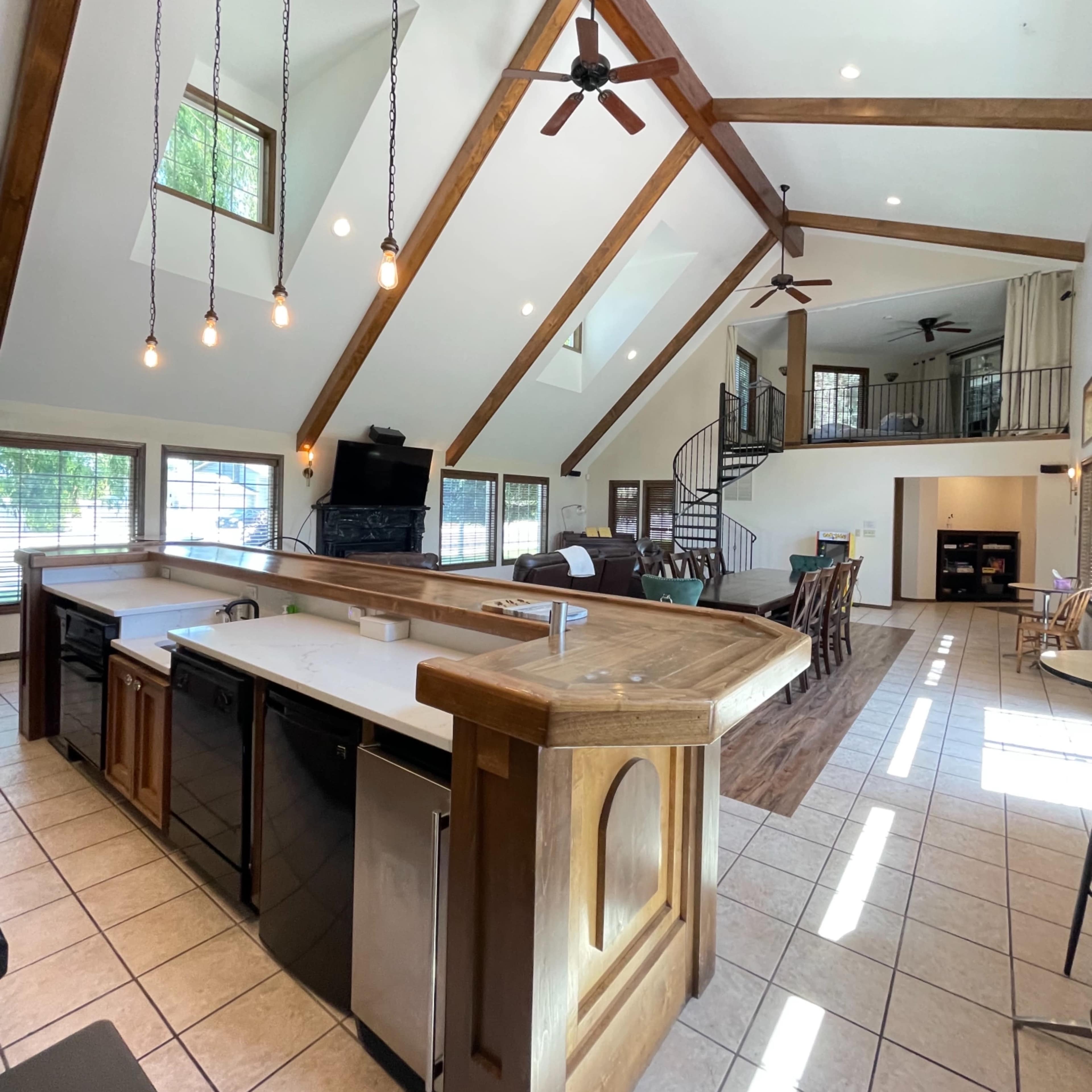 A spacious kitchen with a large island, featuring modern appliances, high wooden beams overhead, and ample natural light entering through large windows.