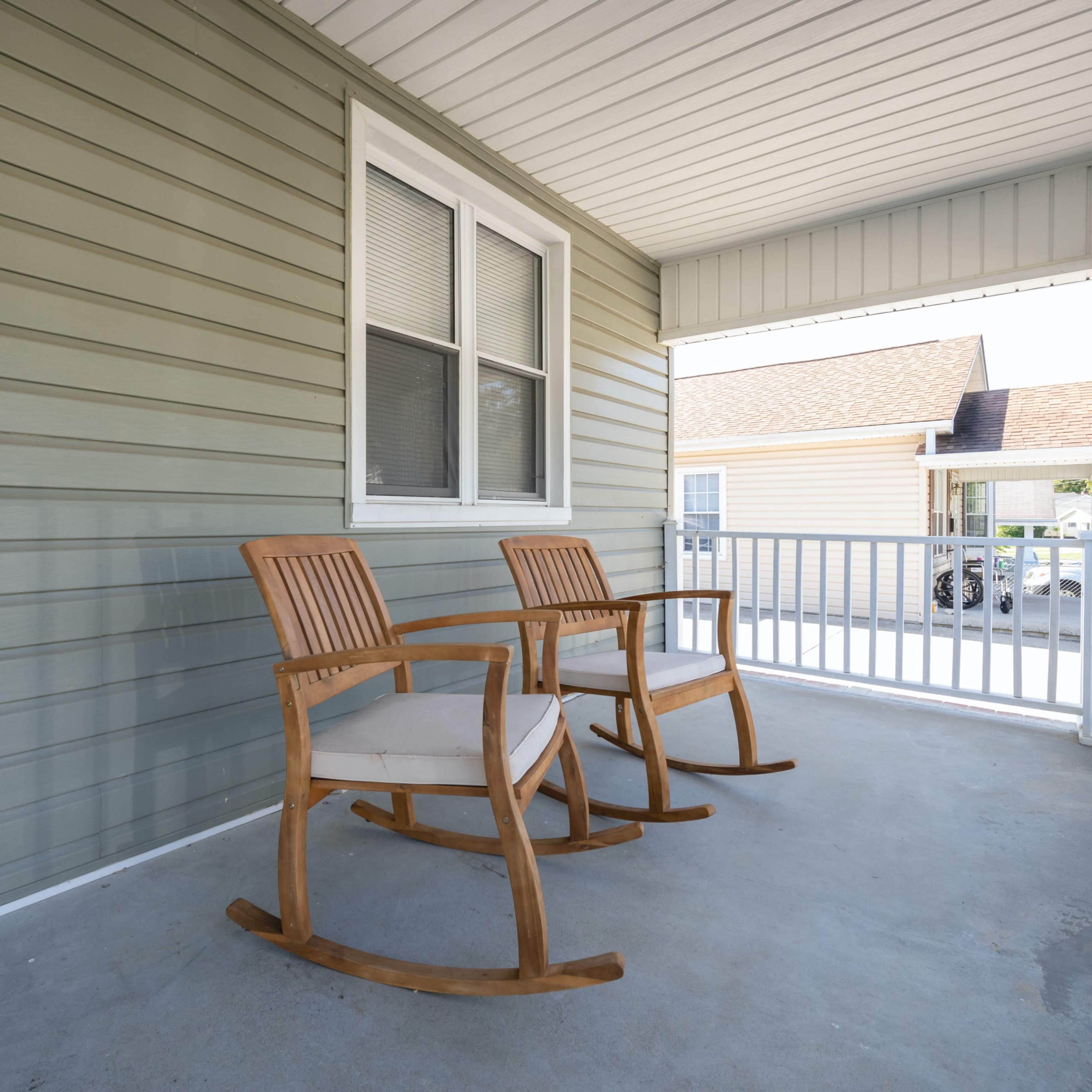 A porch with two wooden rocking chairs positioned side by side against a light green wall.