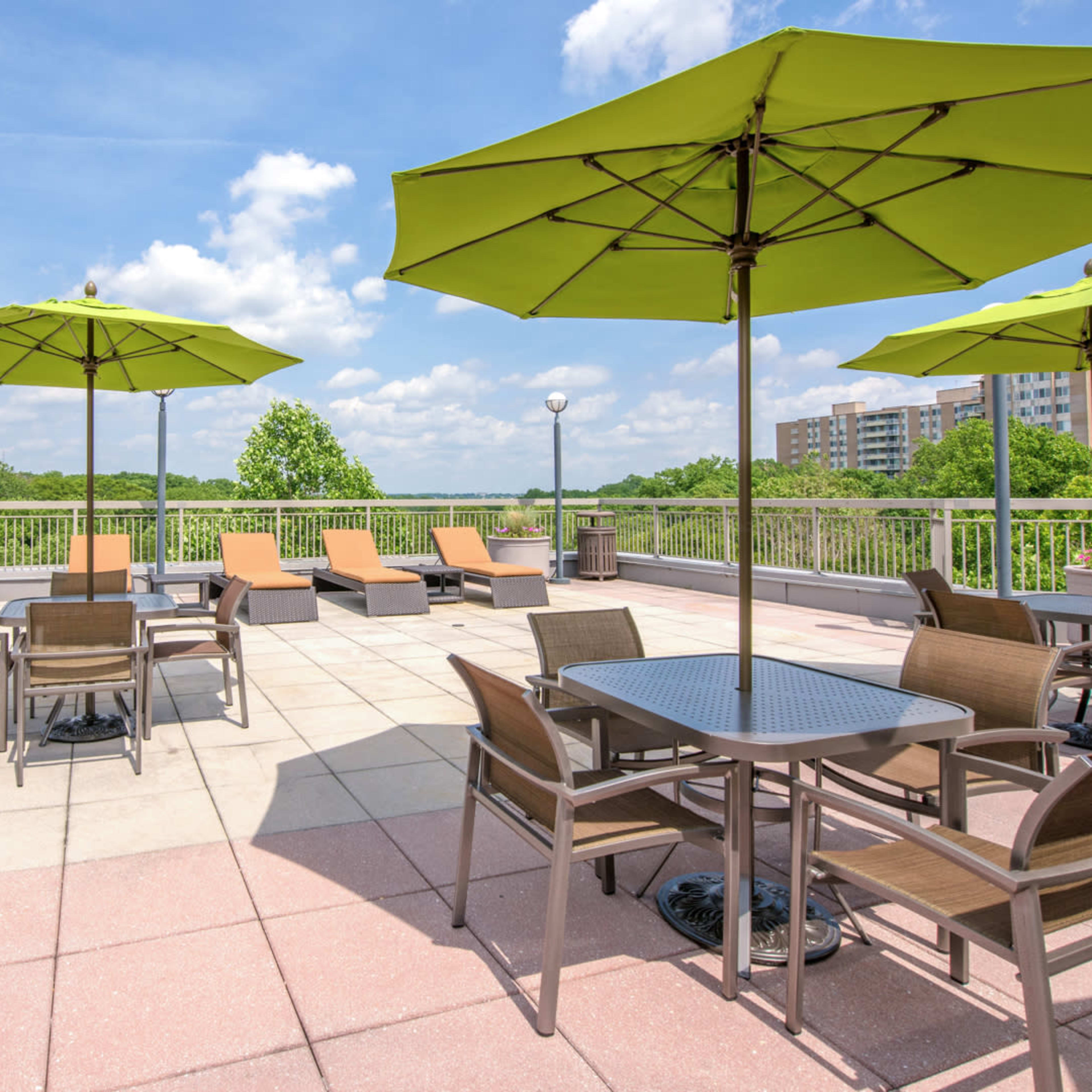 A rooftop terrace with green umbrellas, lounge chairs, and dining tables overlooking a lush landscape.