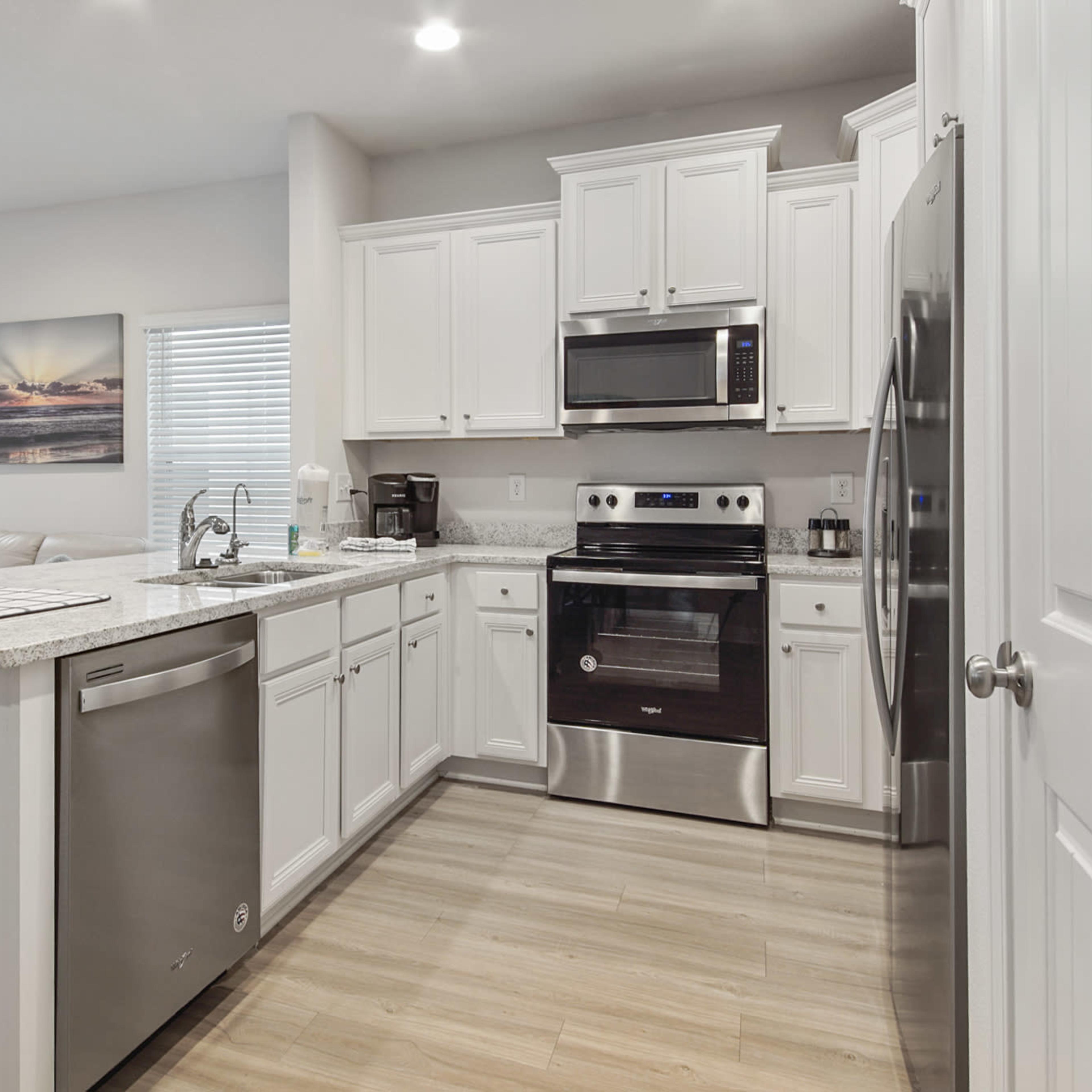 A modern kitchen features white cabinetry, stainless steel appliances, and a view into a living area with a light-colored sofa.
