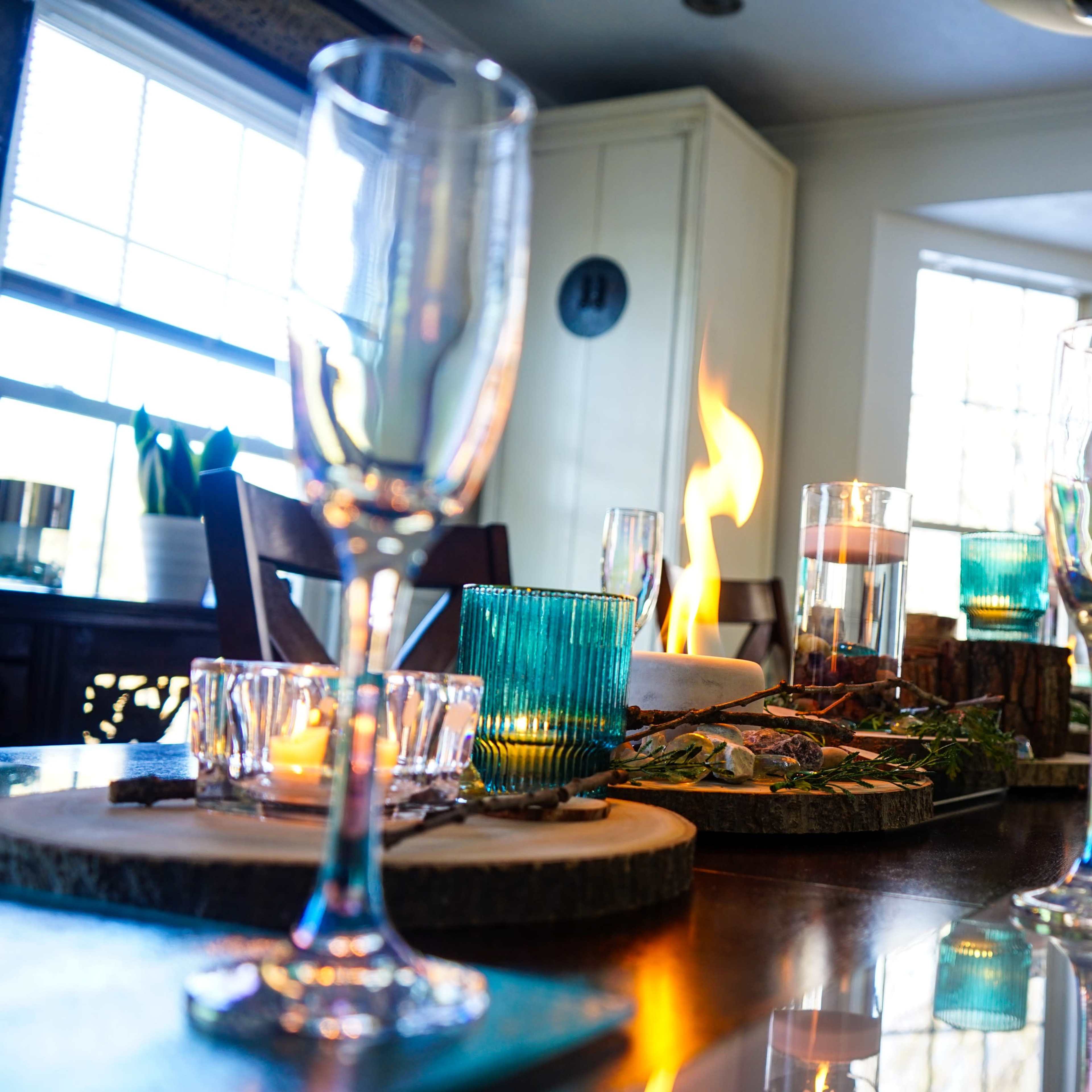 A dining table set with glassware and candles, featuring a centerpiece with flames and decorative elements.