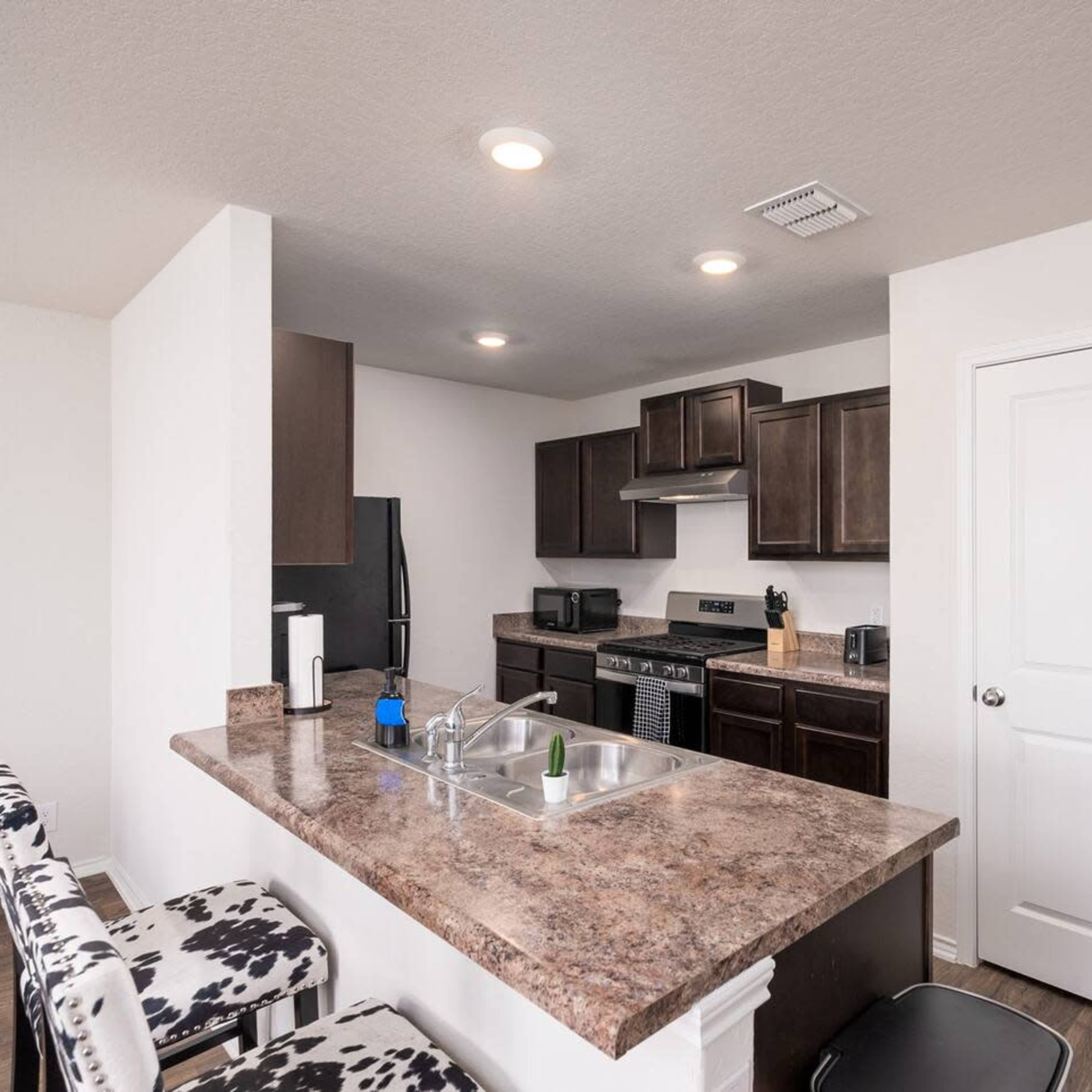 A modern kitchen with dark cabinetry, a stainless steel stove, and bar seating with patterned stools.