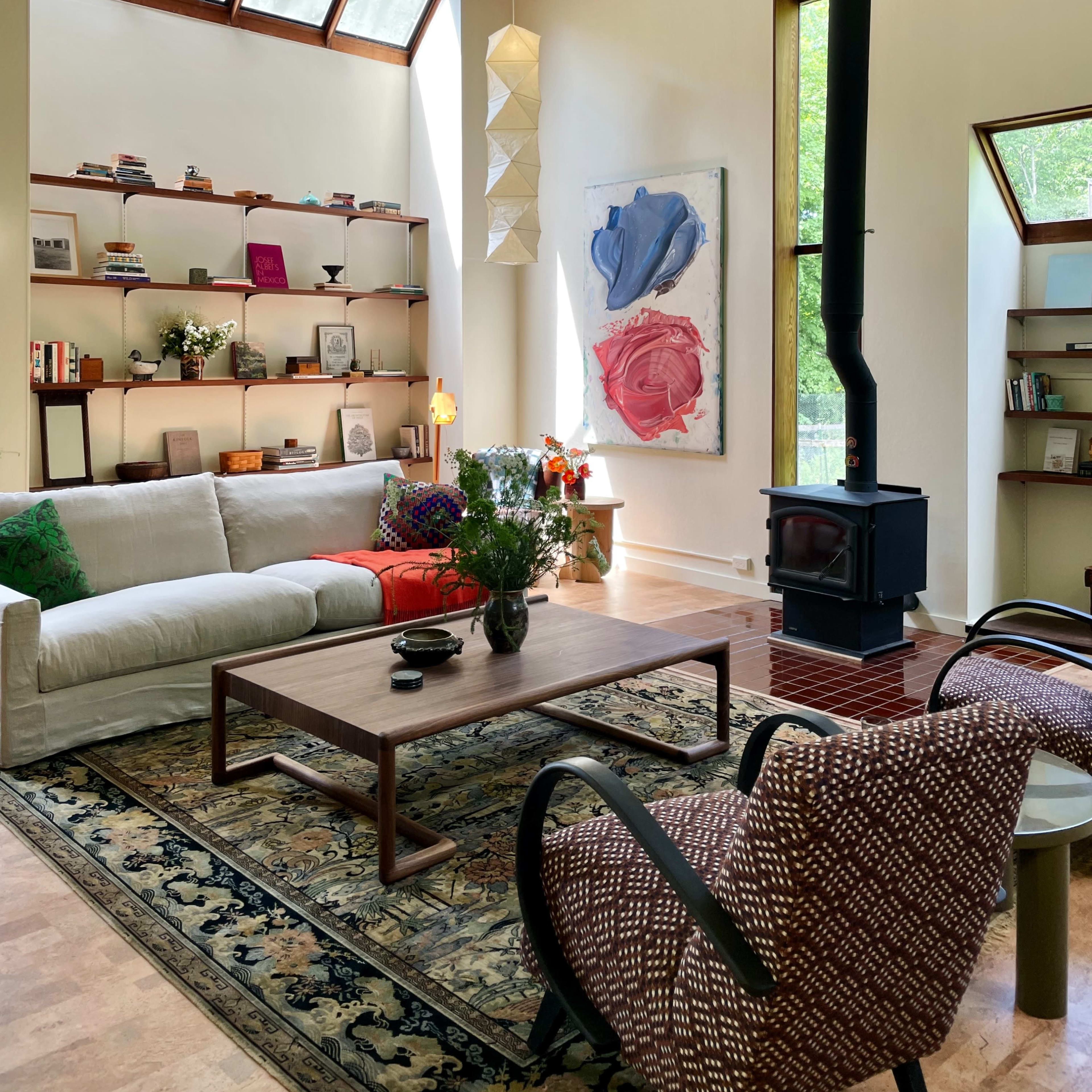 A bright, modern living room features a white sofa, a wooden coffee table, and a wood-burning stove, with shelves filled with books and decorative items.