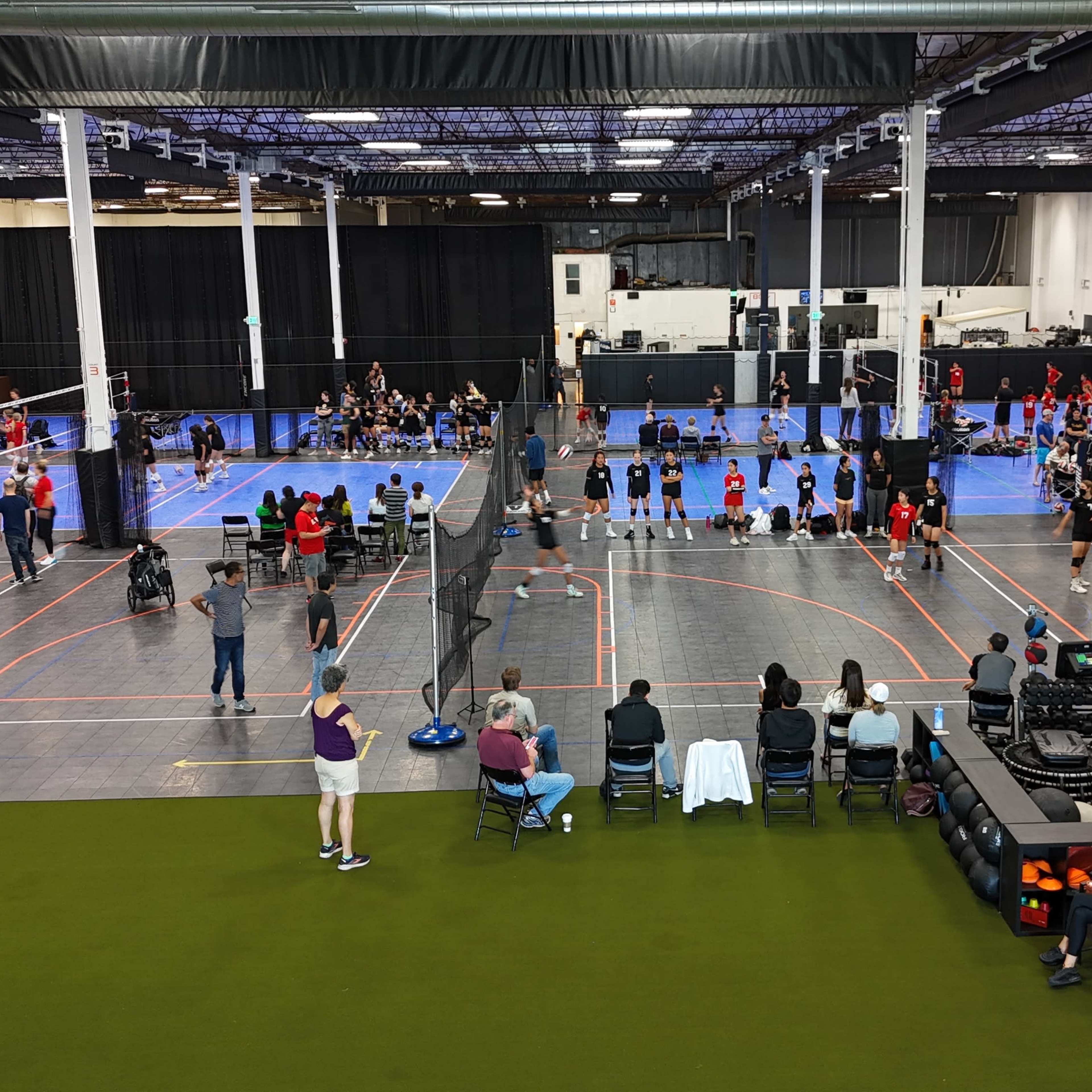 A large indoor sports facility with multiple volleyball courts, where teams are playing and spectators are seated.