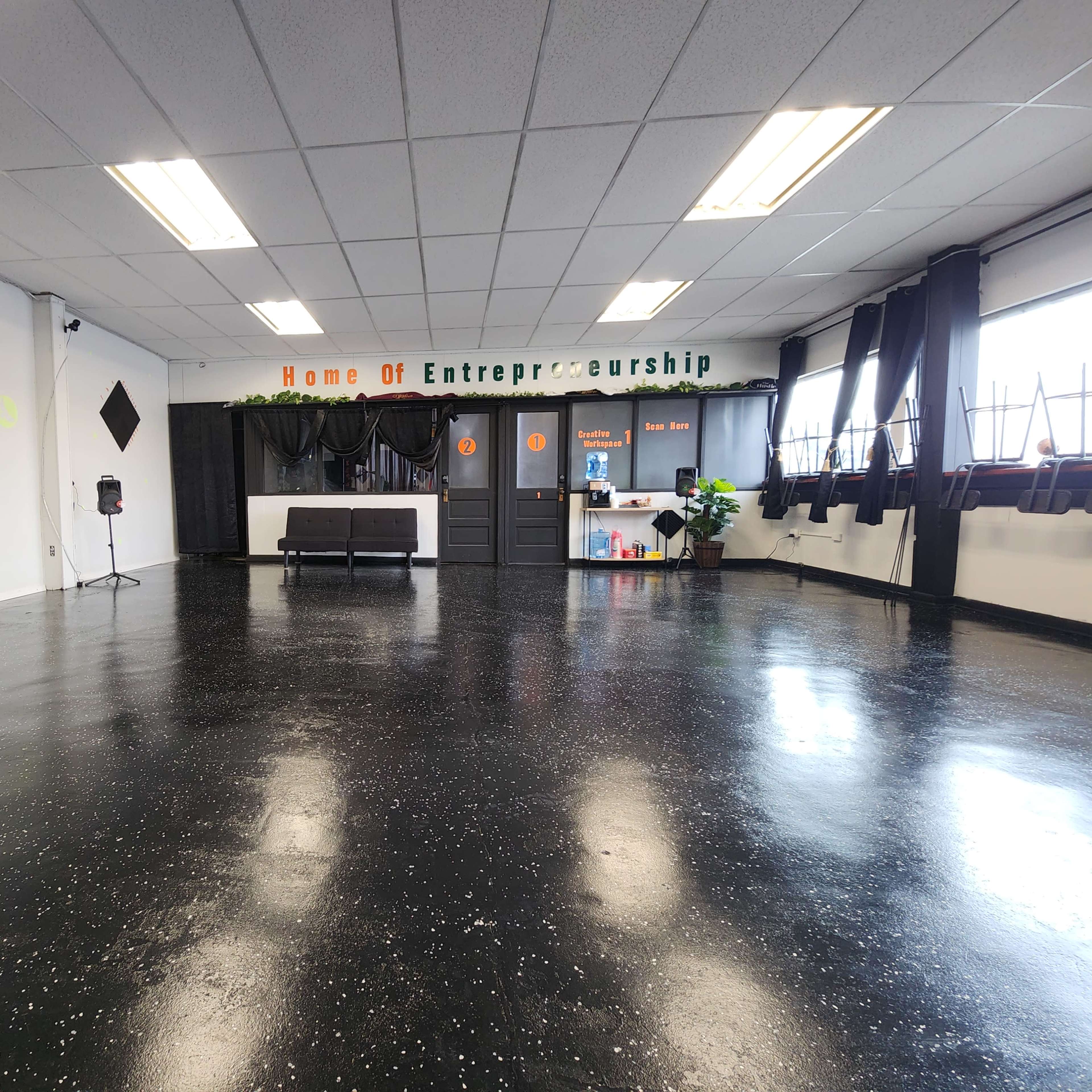 A spacious room with a polished black floor, a waiting area with a couch, and a decorated wall that says "Home Of Entrepreneurship."