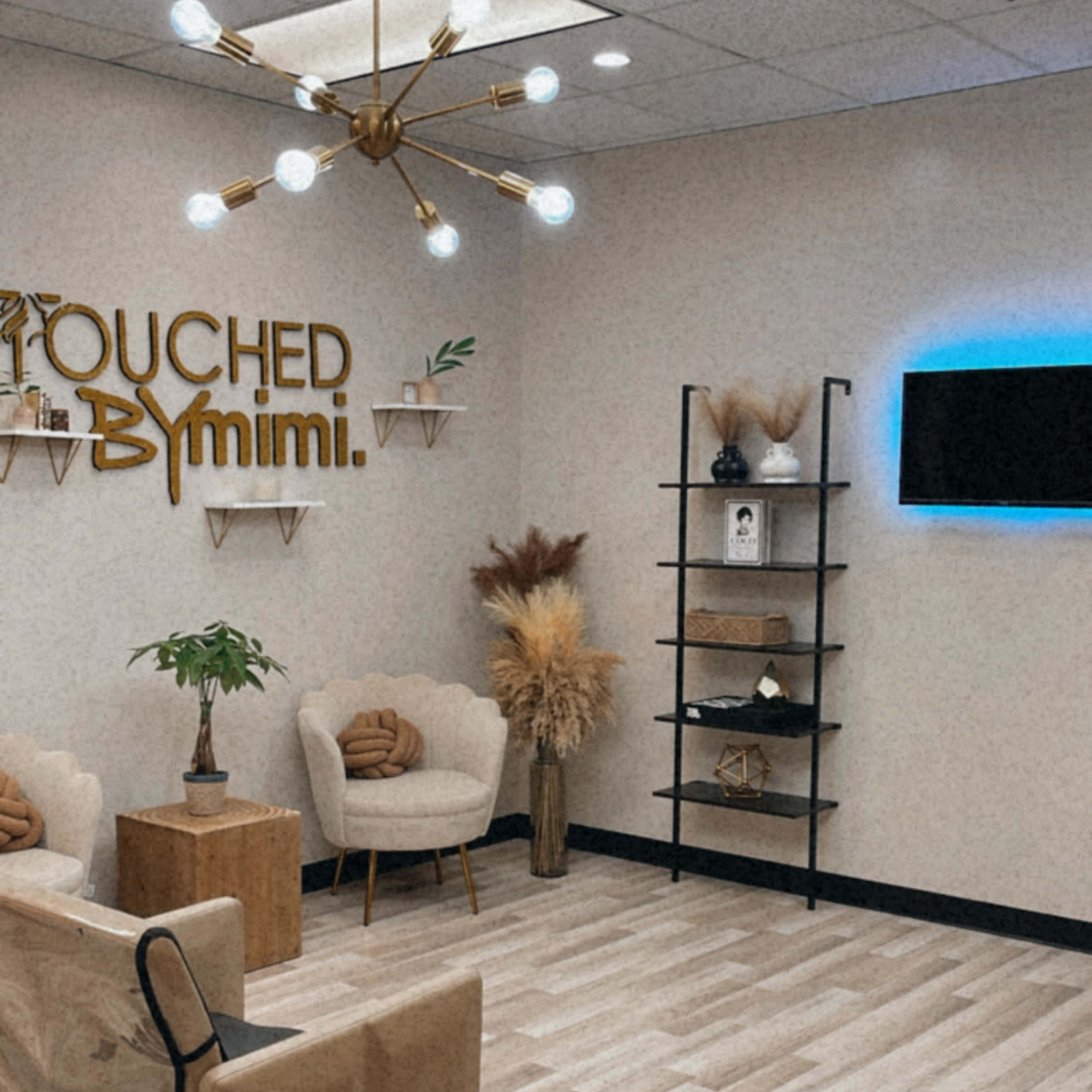A modern salon interior with stylish seating, decorative plants, and a wall sign that reads "TOUCHED BY mimi."