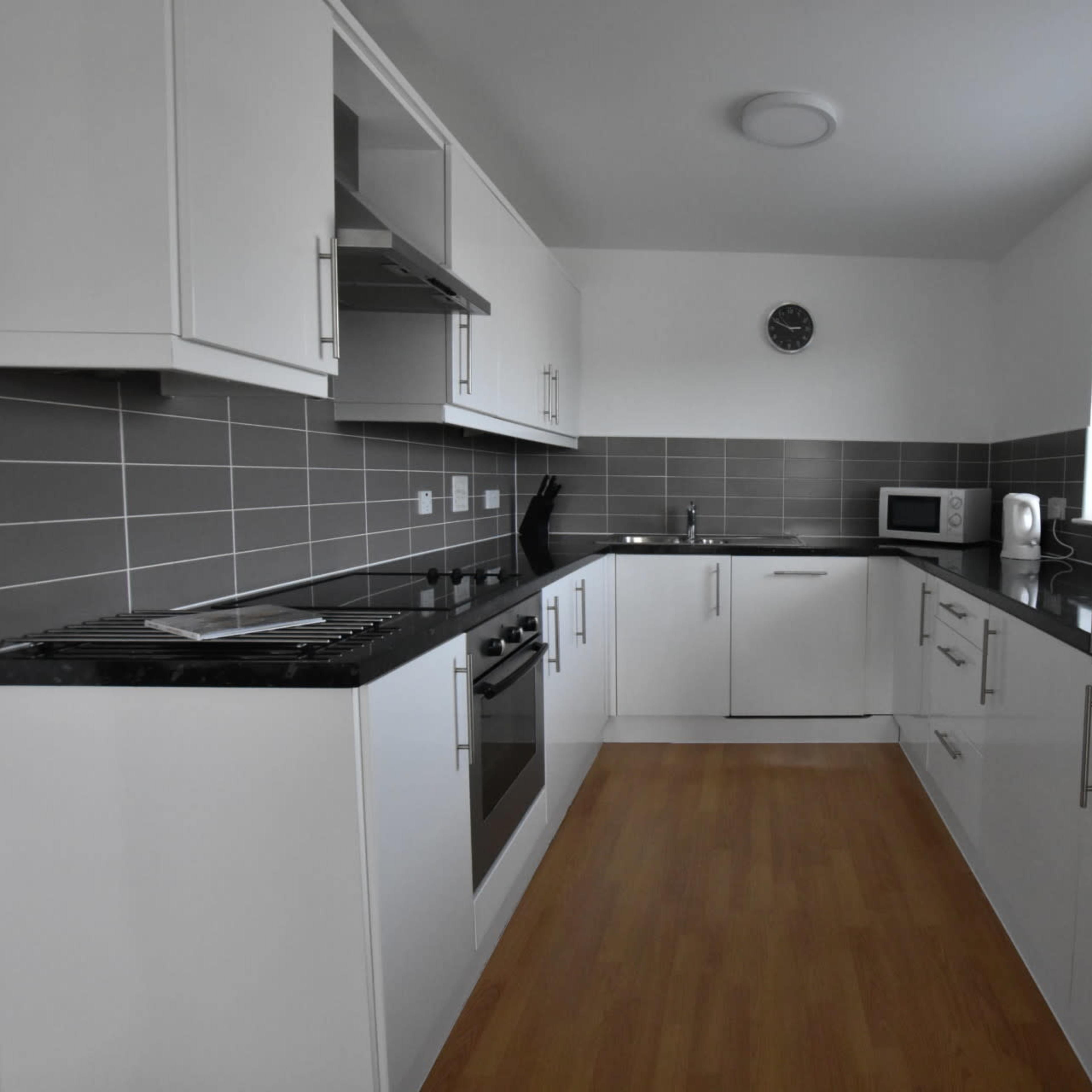 A modern kitchen with white cabinetry, gray tile backsplash, and a wooden floor.
