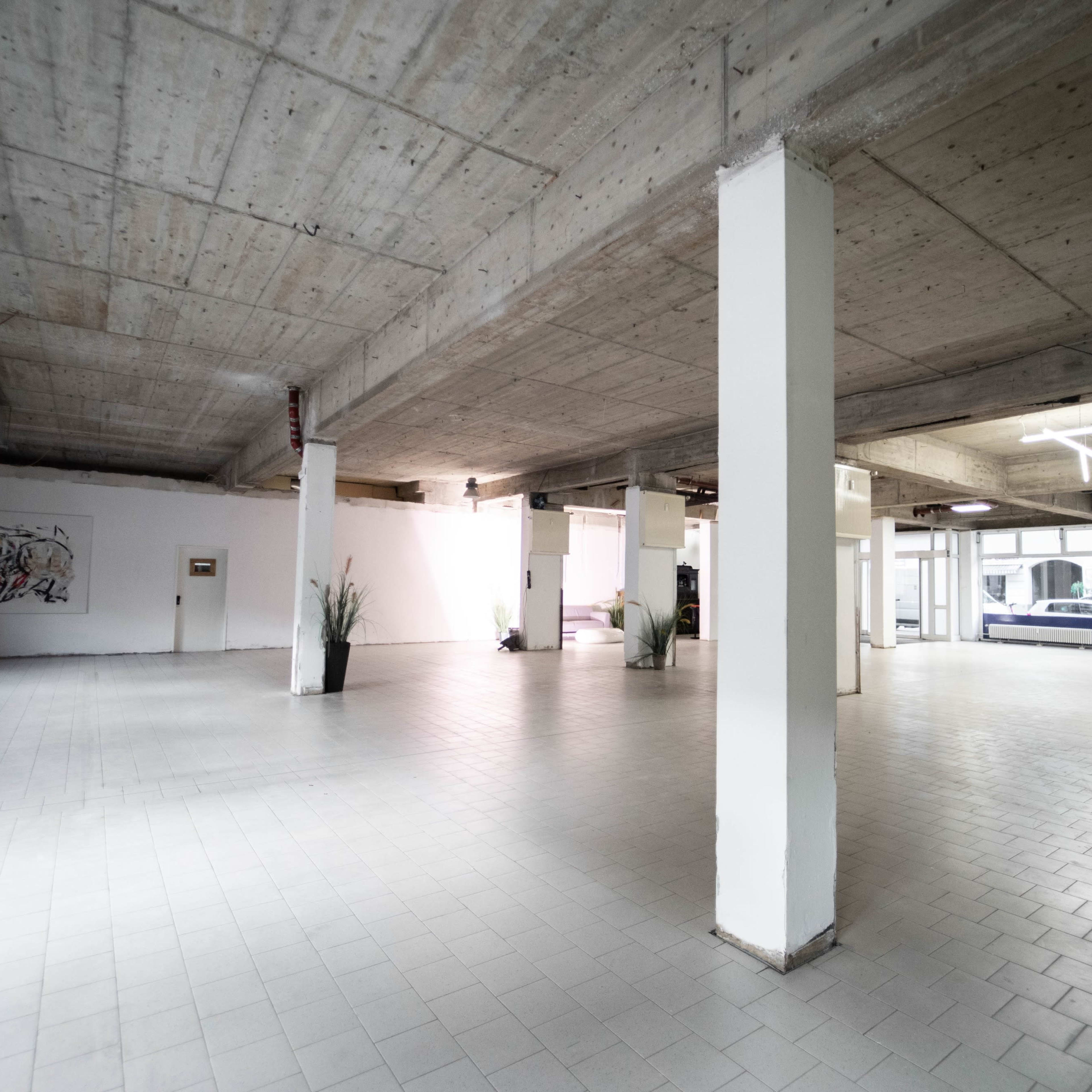 A spacious, empty interior with concrete ceilings and tile flooring, featuring several pillars and minimal decorative elements.
