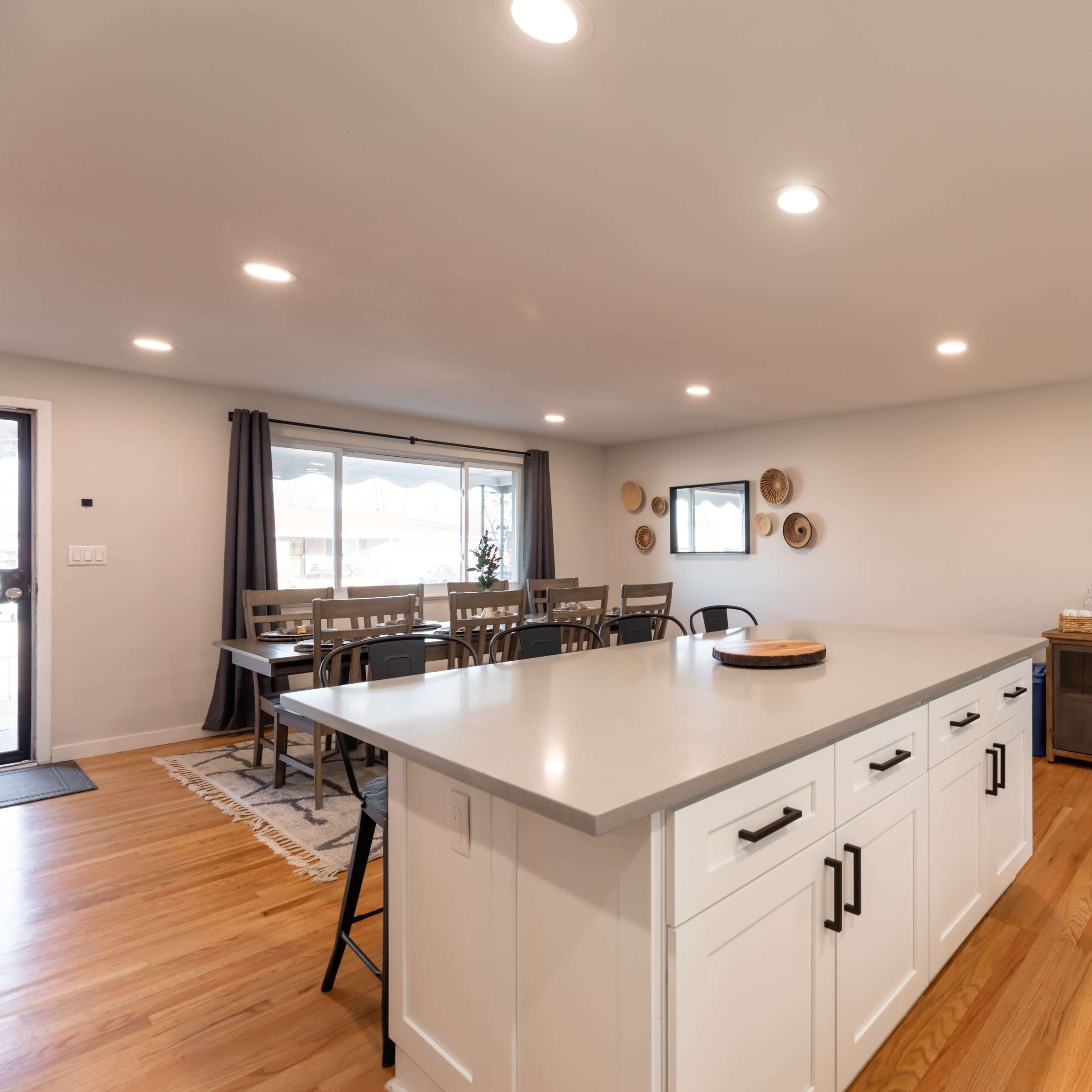 A modern kitchen and dining area features a large island with white cabinetry, hardwood floors, and simple decor elements on the walls.